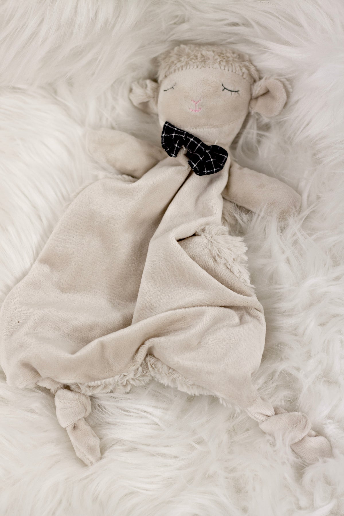Liam the Lamb comforter lying on soft white faux fur