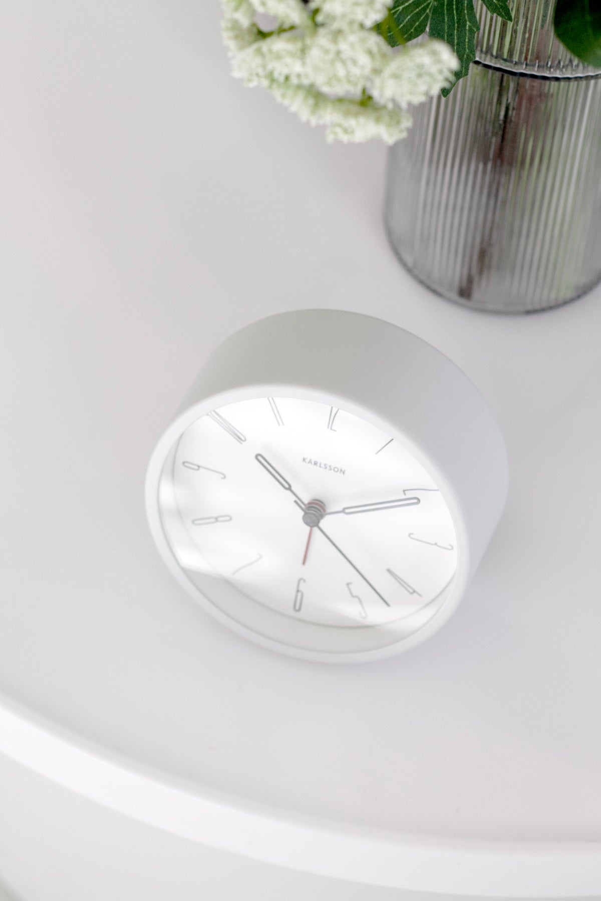 White Belle alarm clock on a round white table beside a plant in soft light