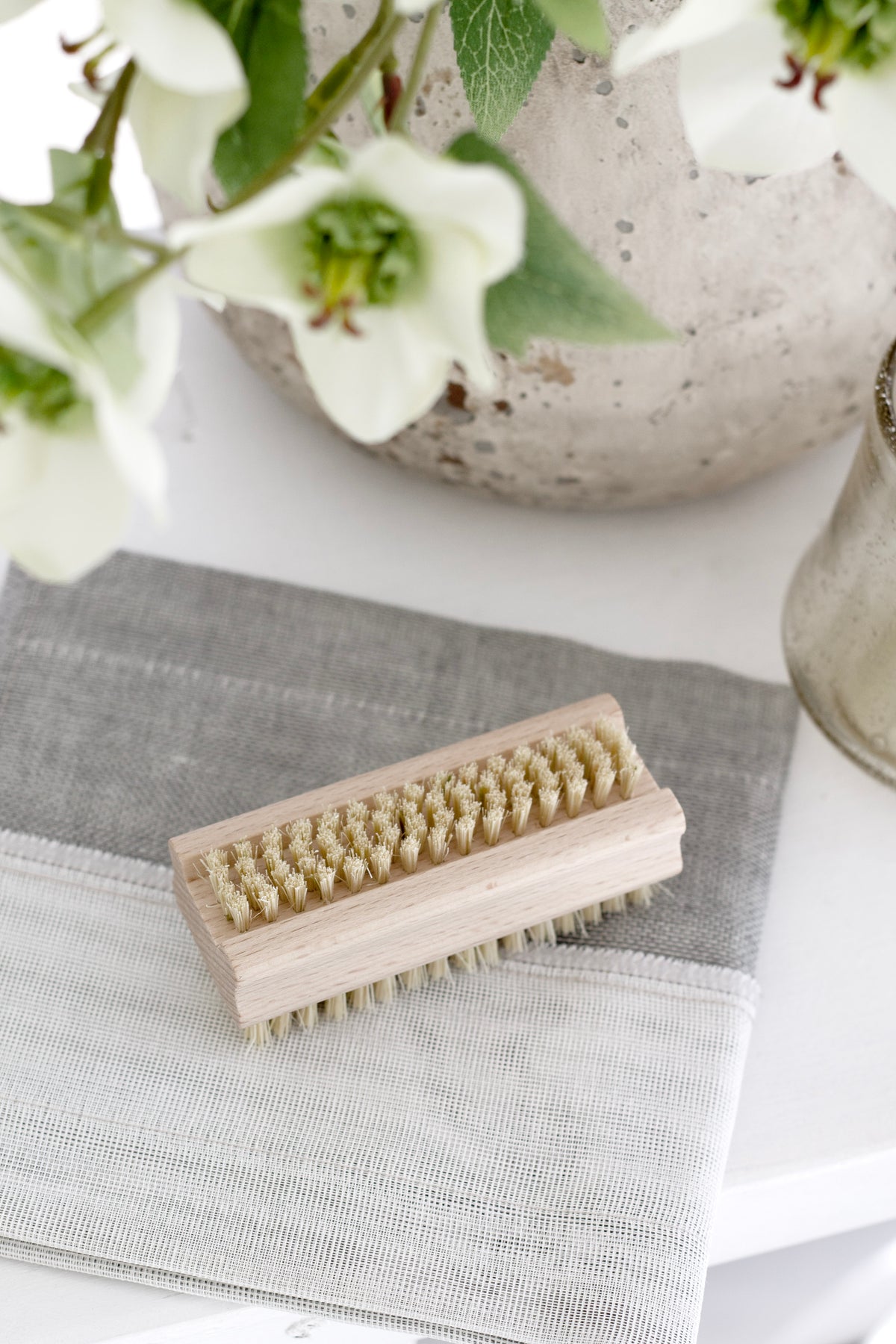 Nail brush on a folded grey cloth beneath white flowers