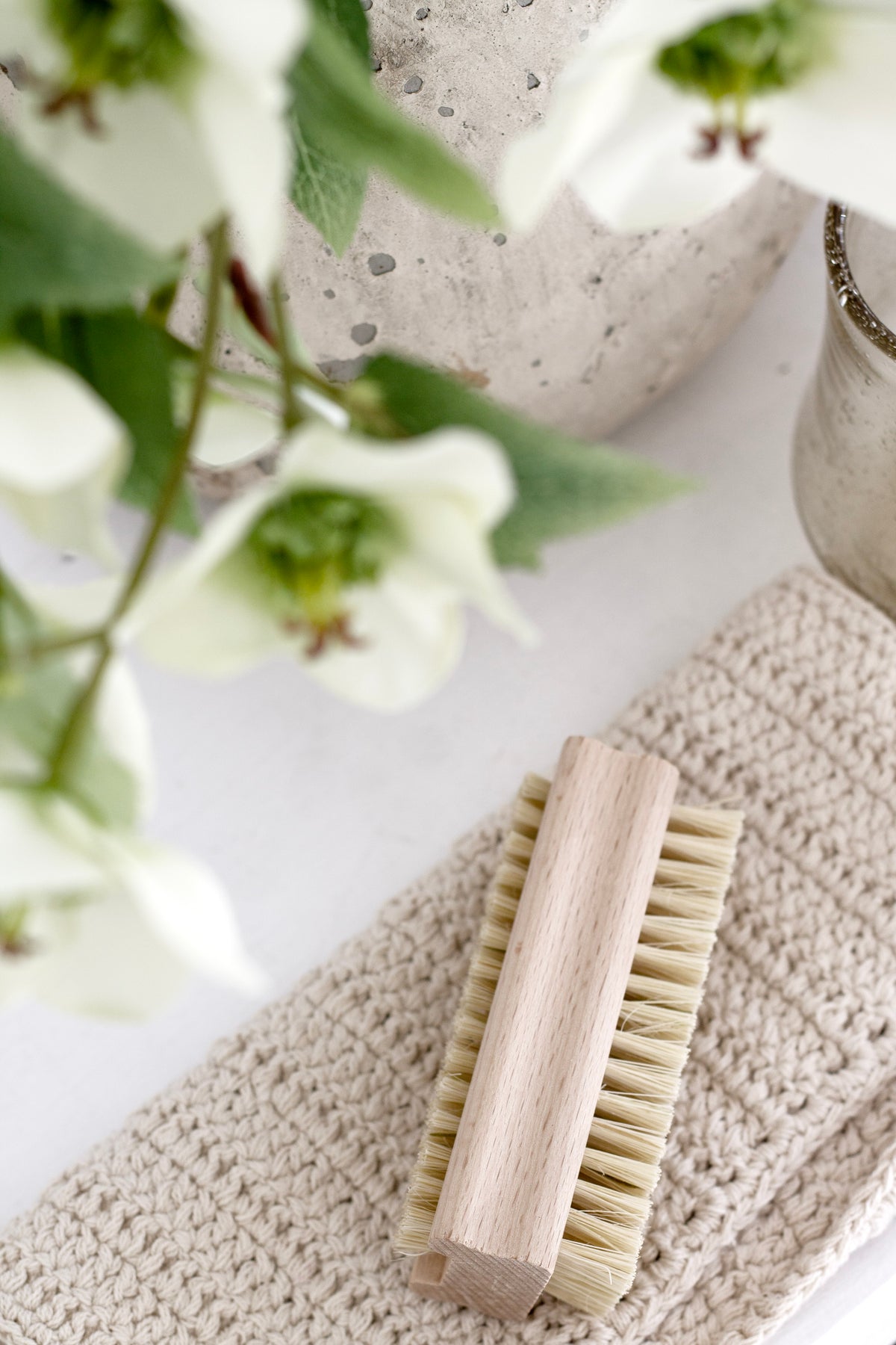 Beechwood nail brush on a knitted cloth beside white flowers