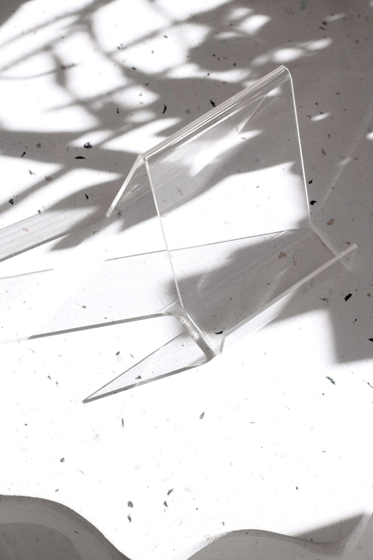Acrylic book stand empty on a speckled surface, dappled light through the clear panels
