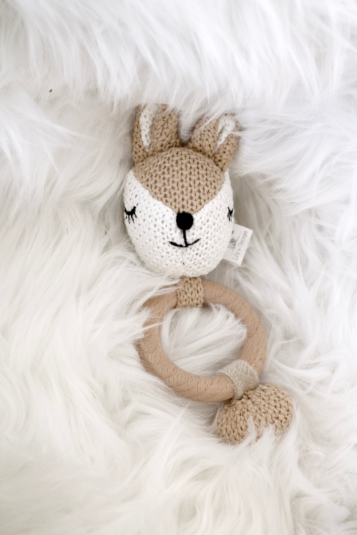 Miss Deer crocheted teether lying on a white faux fur throw