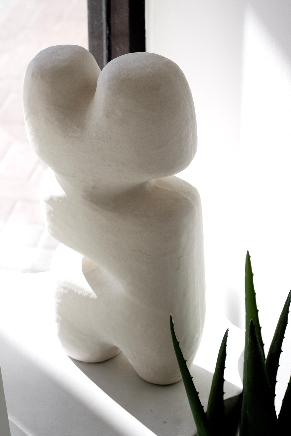 Block sculpture on a window ledge beside an aloe, side light across the surface