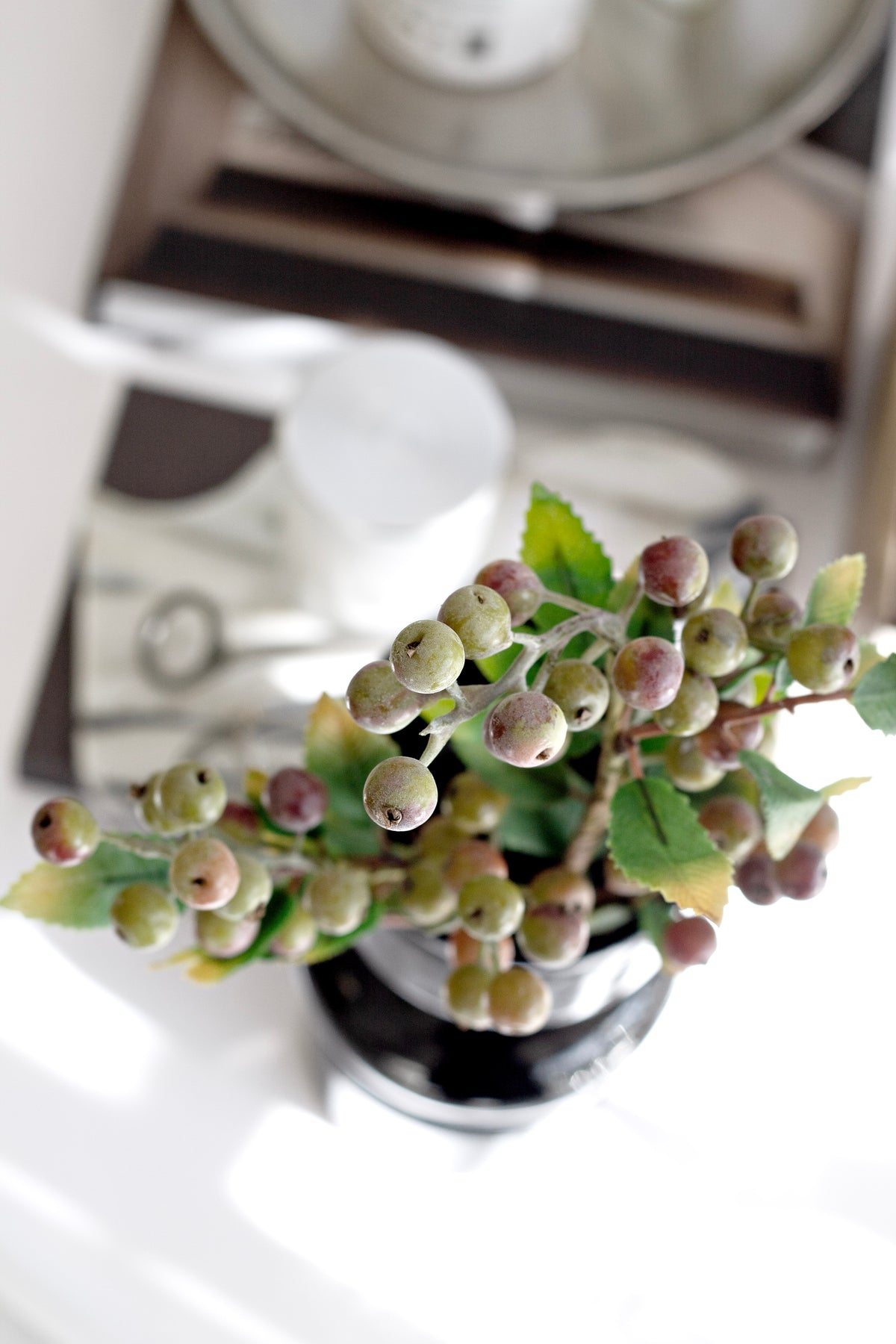 Faux summer berry branch arranged in a dark vase on a kitchen bench
