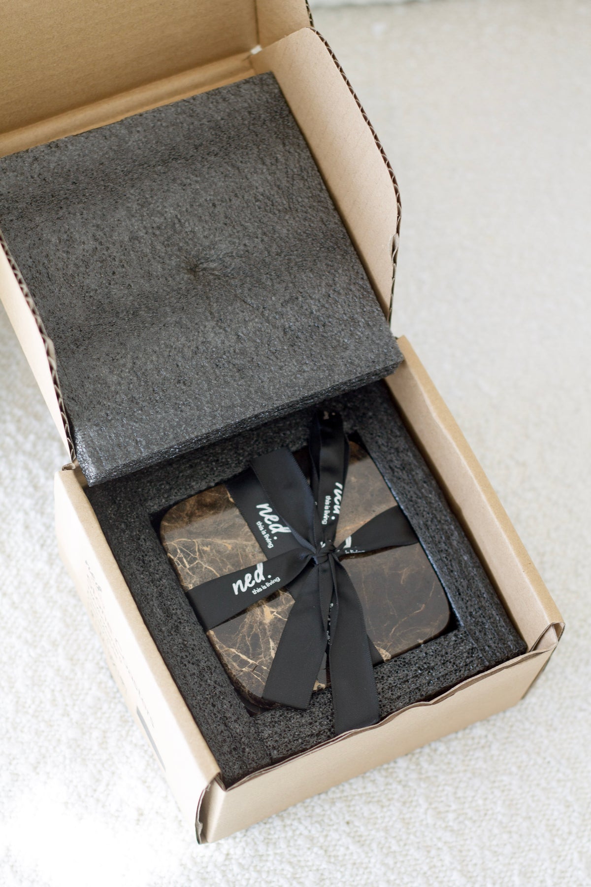 Stone coaster gift box open on a white surface, coasters tied with a black ribbon