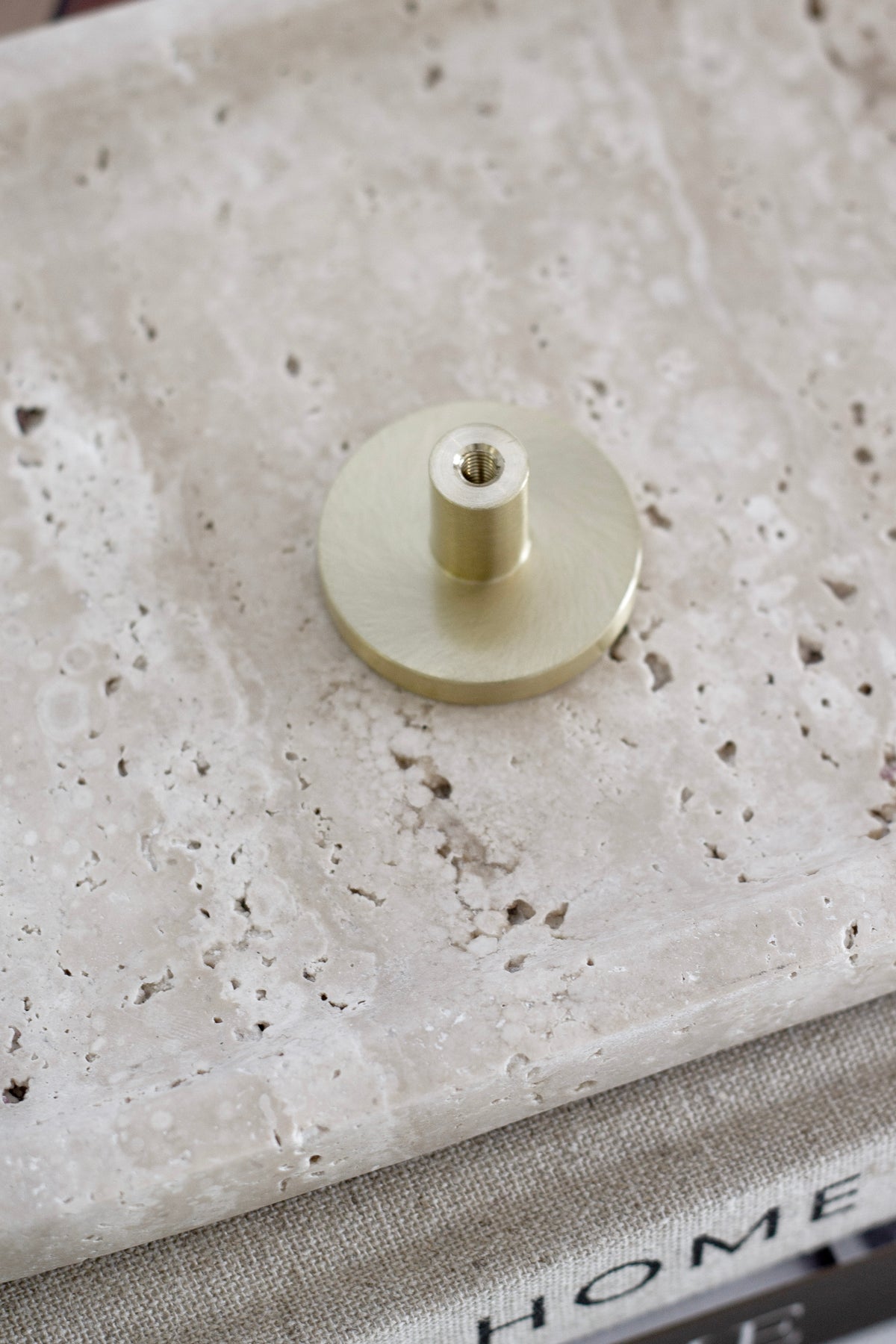 Back of the brass wall hook showing its threaded fixing post on travertine
