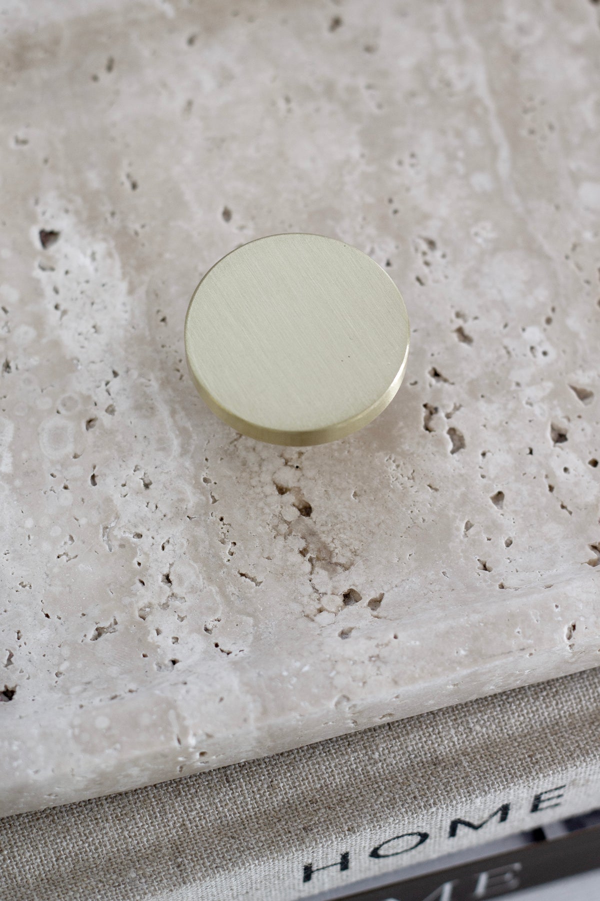 Round face of the brushed gold brass wall hook on a travertine tray