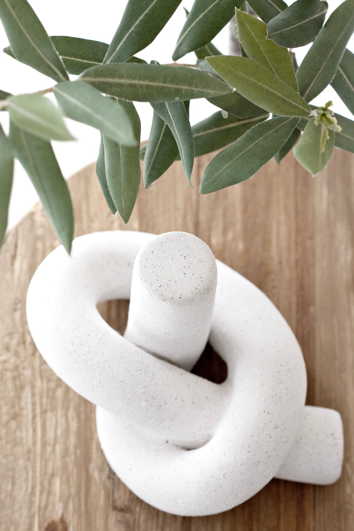 White Knot Ornament on a timber board with olive foliage overhead