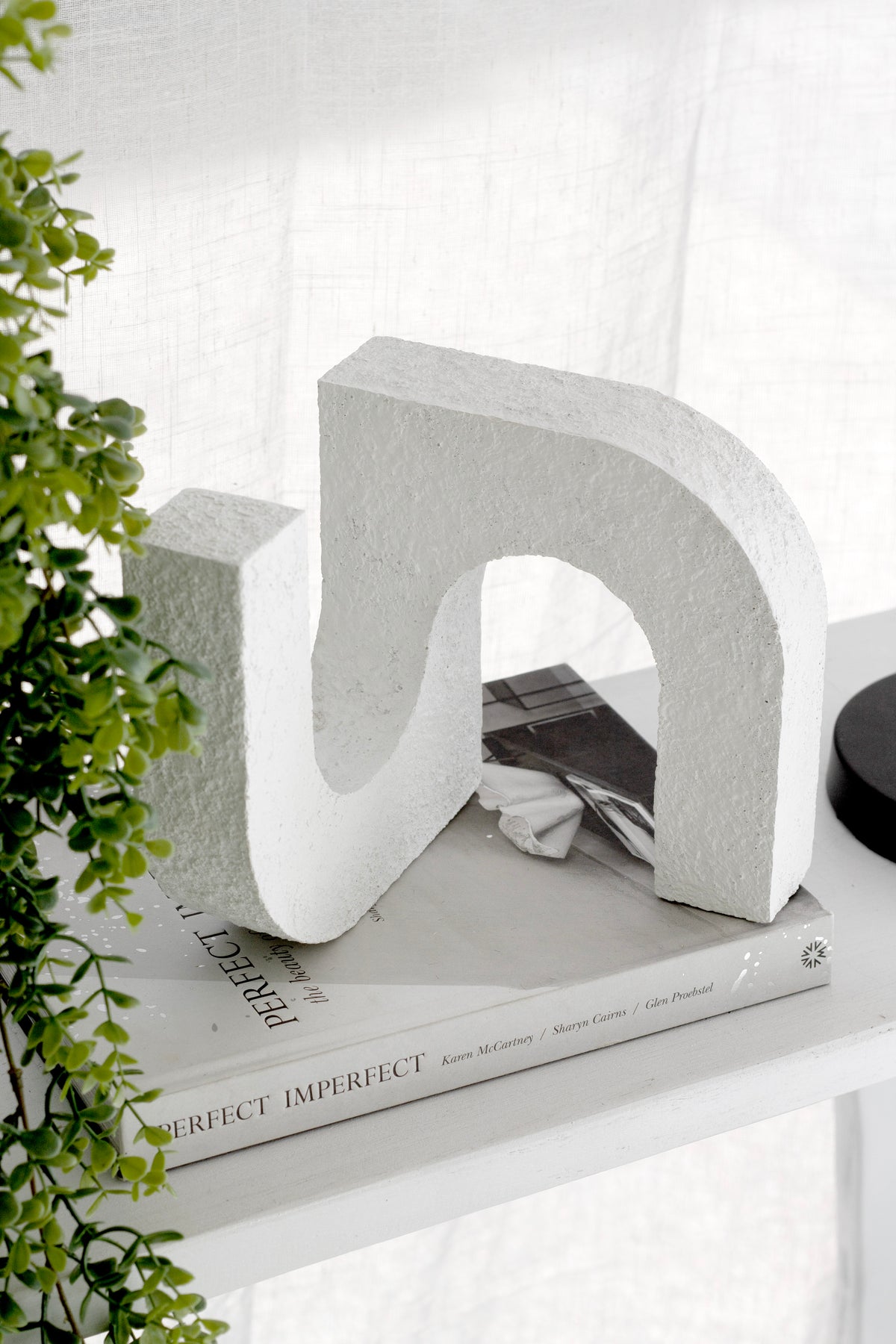 Arch ornament angled on a book beside a dark dish, greenery framing the left