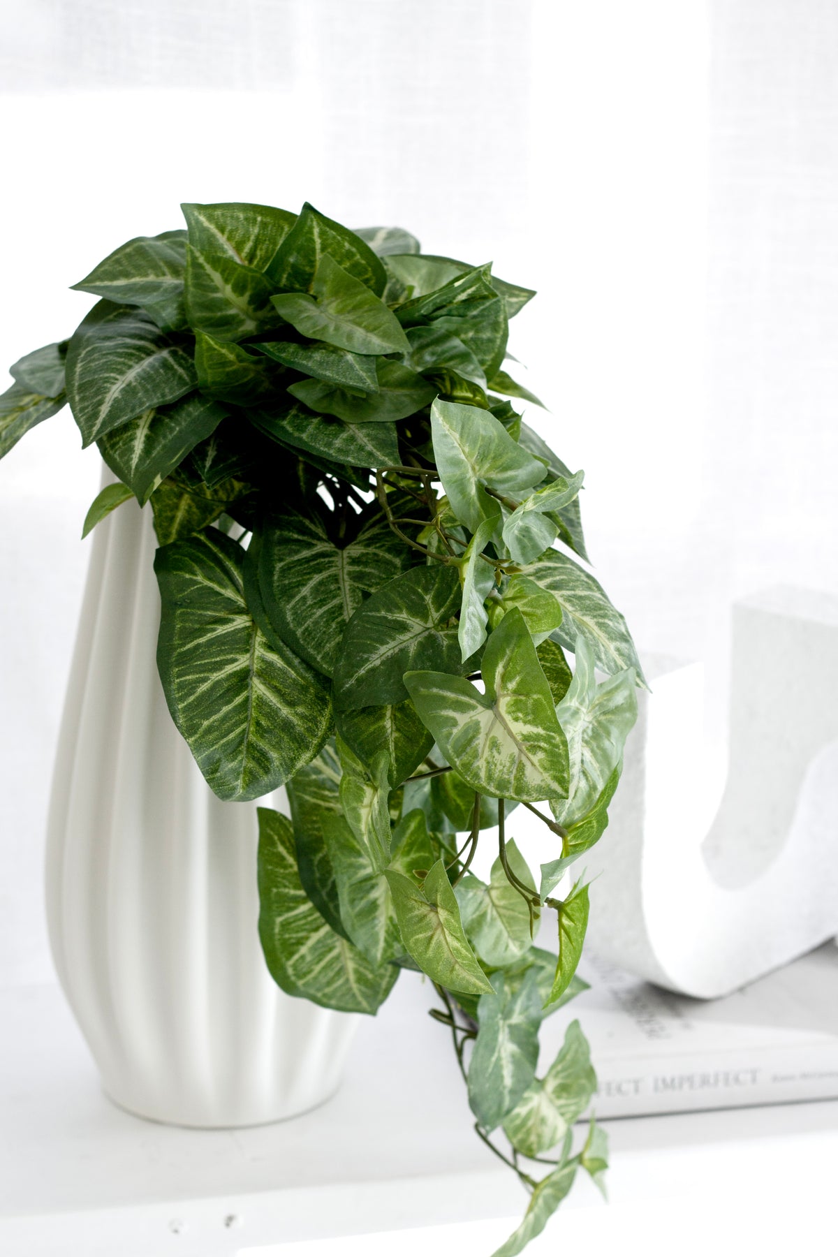 Faux Nephthytis spilling from a white fluted vase beside a white sculpture