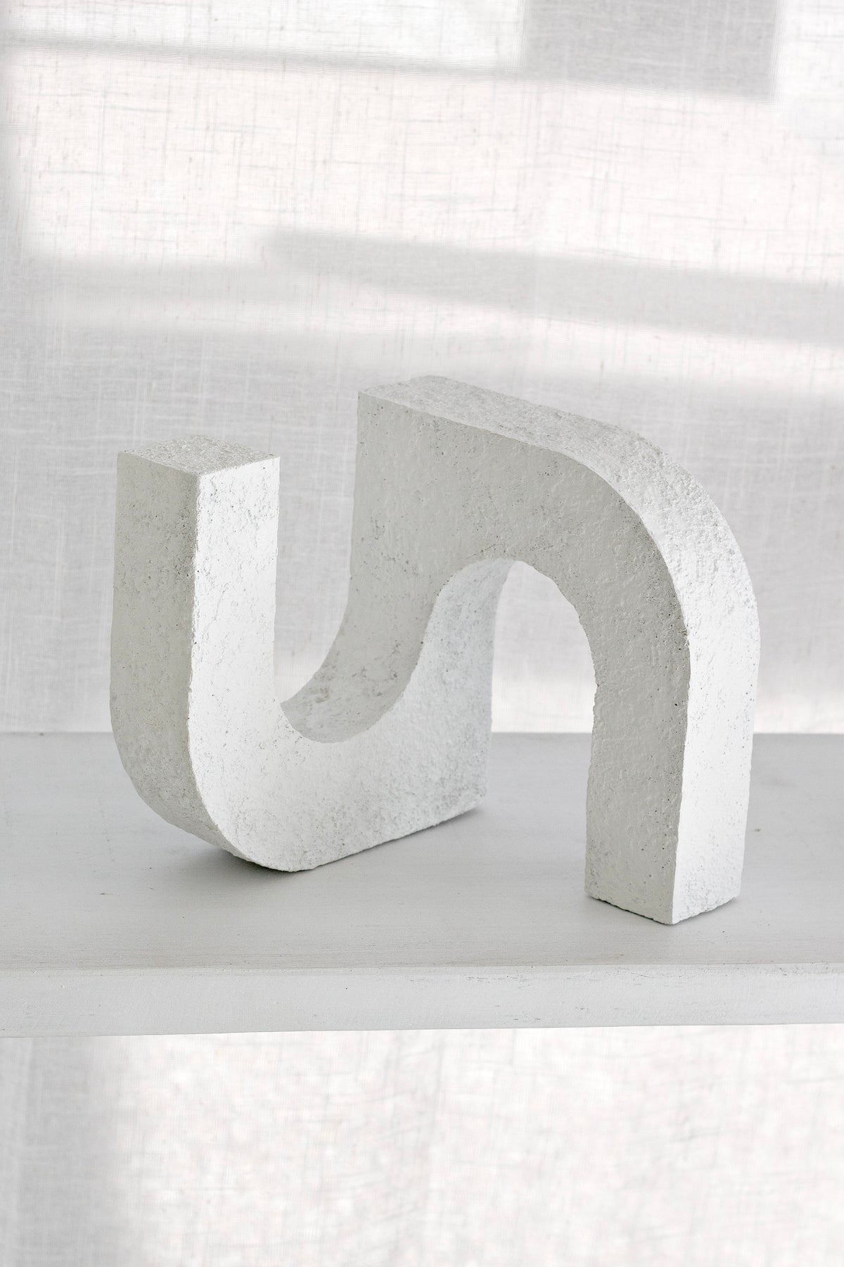 Arch ornament on a white ledge against a linen curtain, openings catching shadow