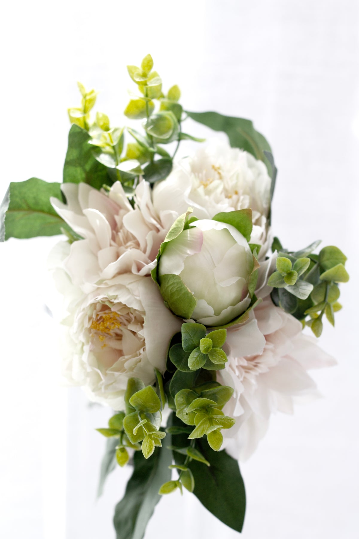 Close view of cream peonies and blush dahlias with green foliage in the faux bouquet