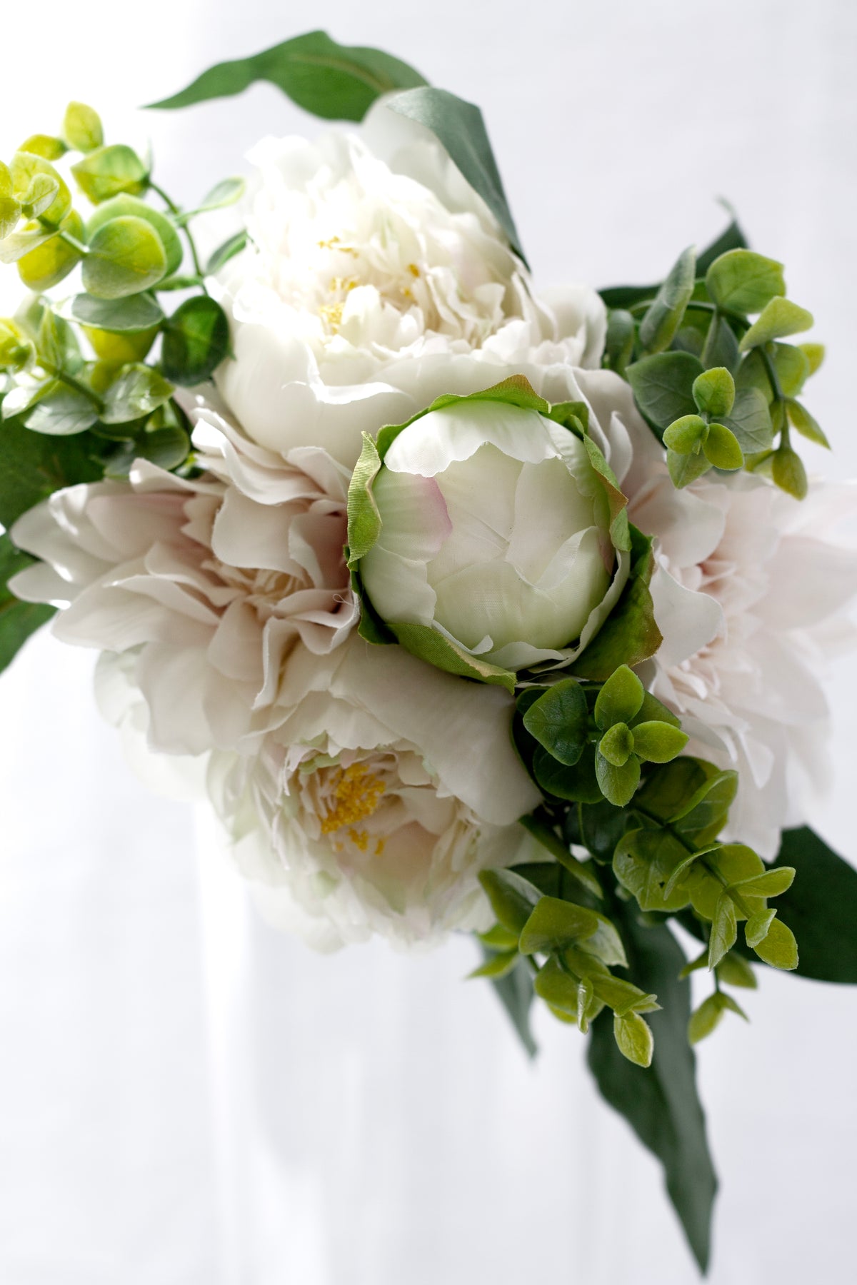 Close-up of cream faux peonies, a peony bud and blush dahlias with green foliage