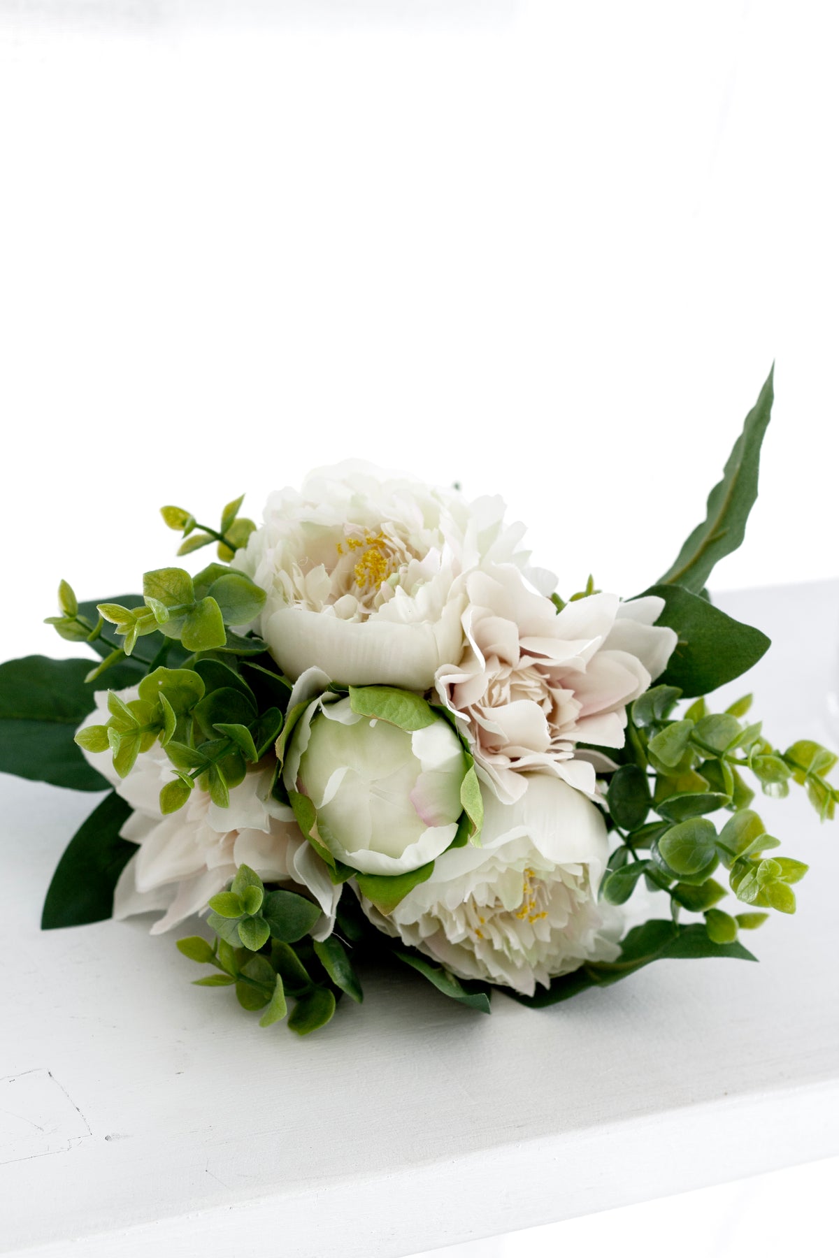 Faux dahlia and peony bouquet set low on a white bench in soft light