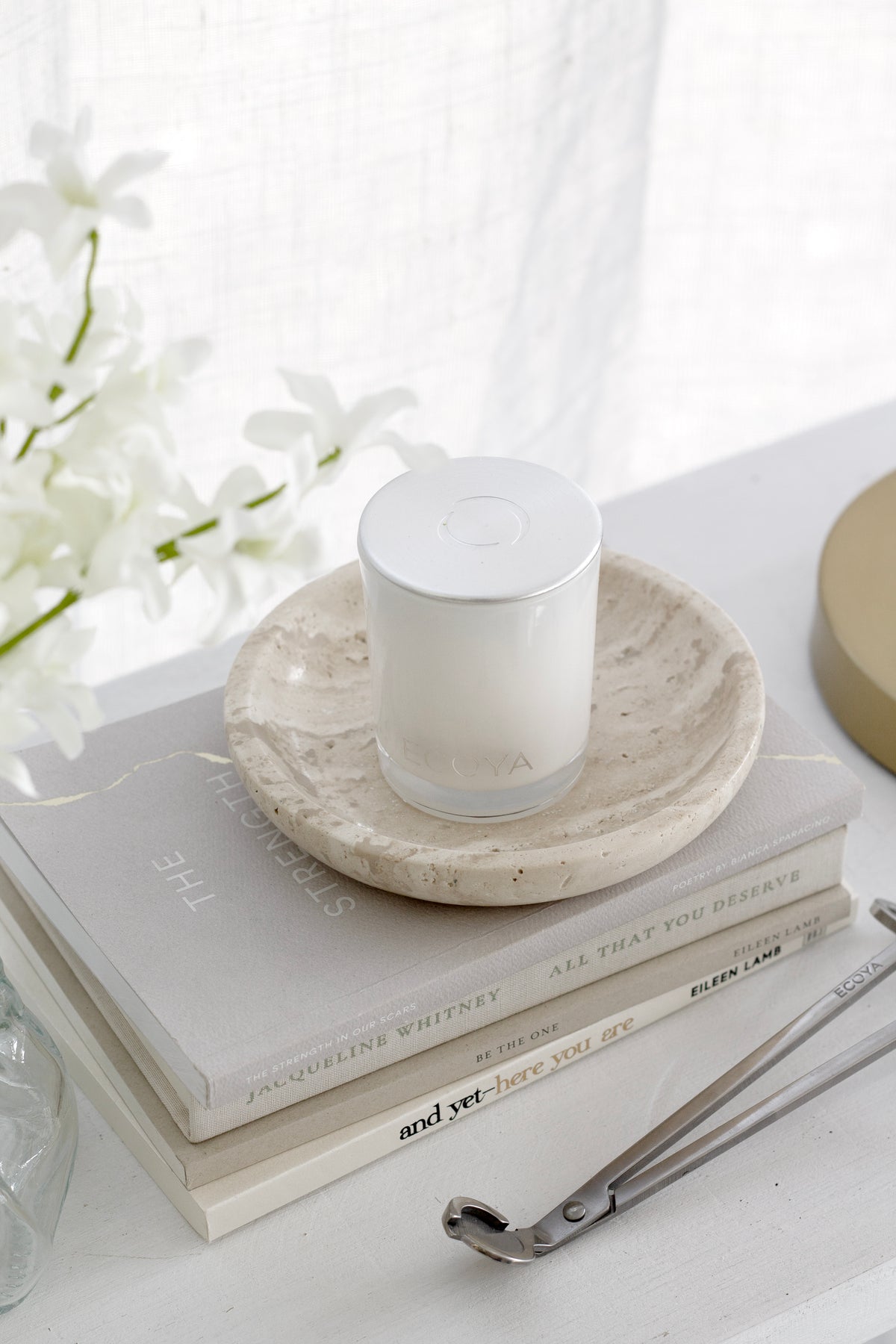 Clear crinkle vase of white blooms at a shelf edge with a candle on a travertine dish