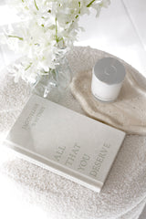 Book titled 'All That You Deserve' with a candle and flowers on a textured surface
