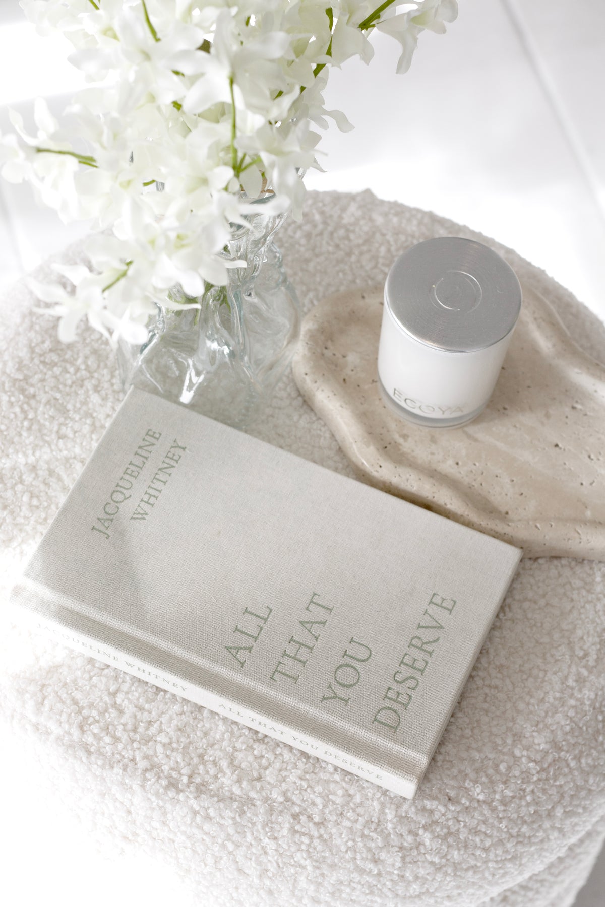 Candle on the travertine tray, resting on boucle with a book and white blooms