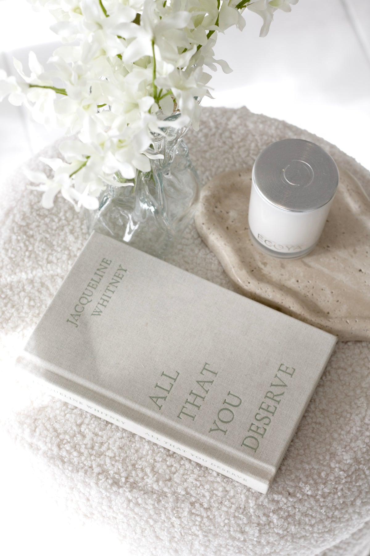 Overhead of the candle and tray on boucle, a book and white stems alongside