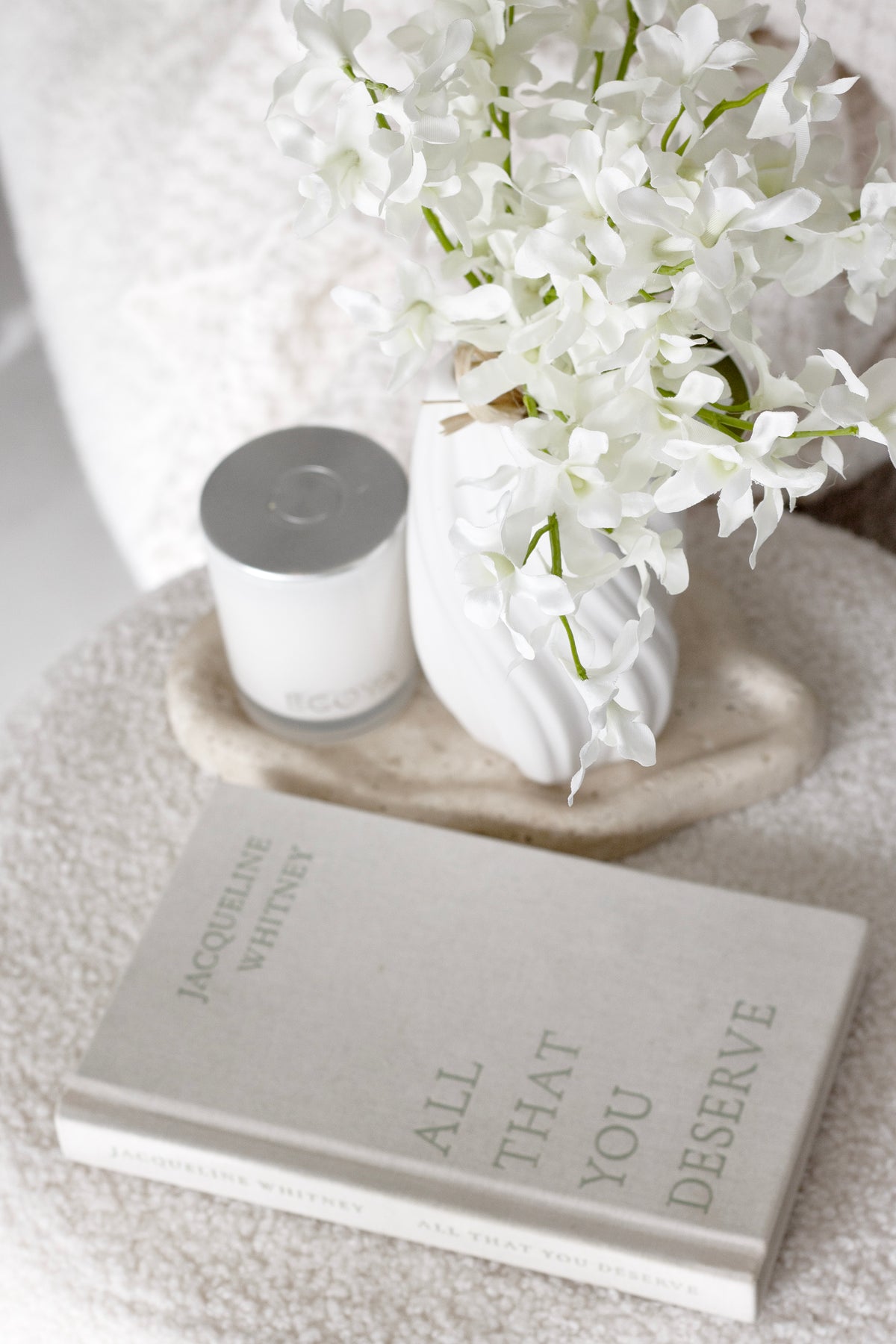 Faux orchids beside a candle and a book on a textured surface