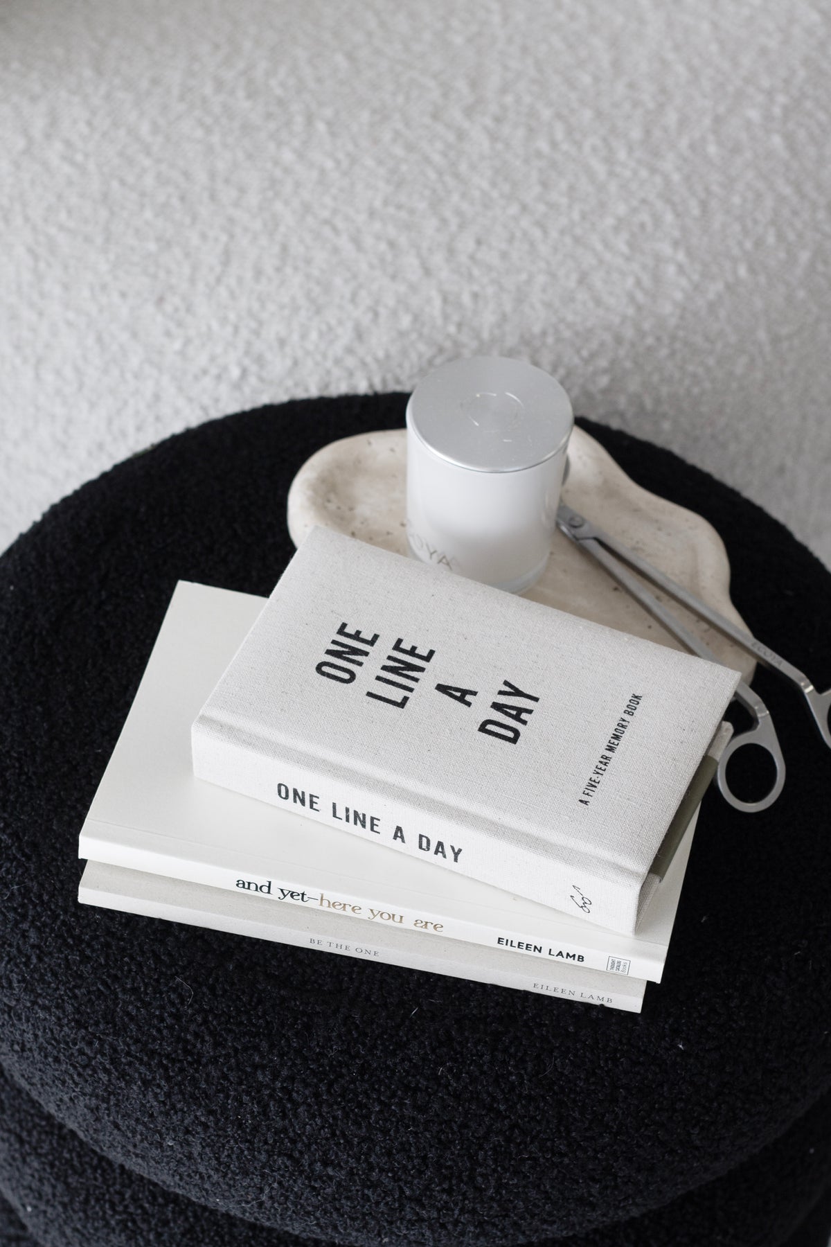 Books and a candle set on a dark round top used as a bedside surface