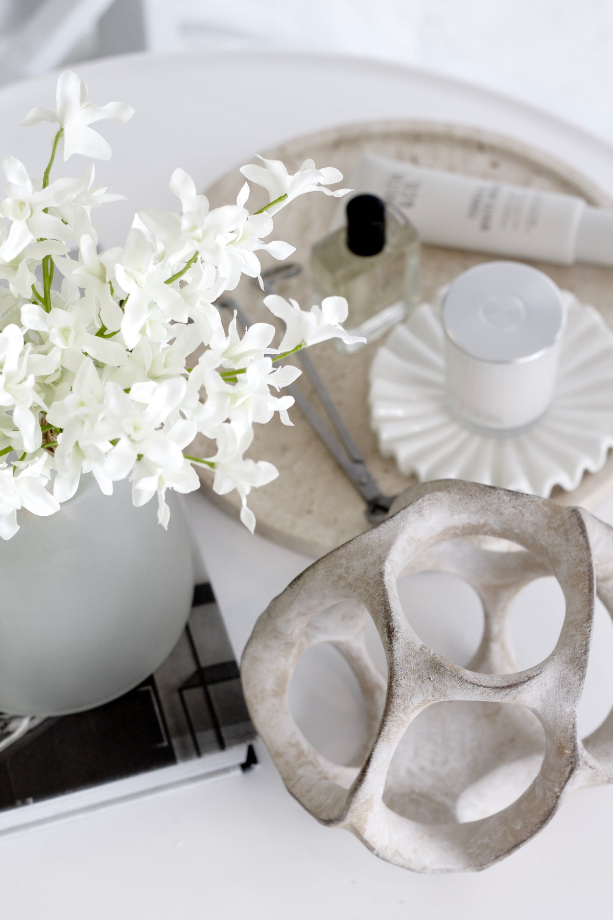 Faux orchids with green leaves in a white sculpted vase