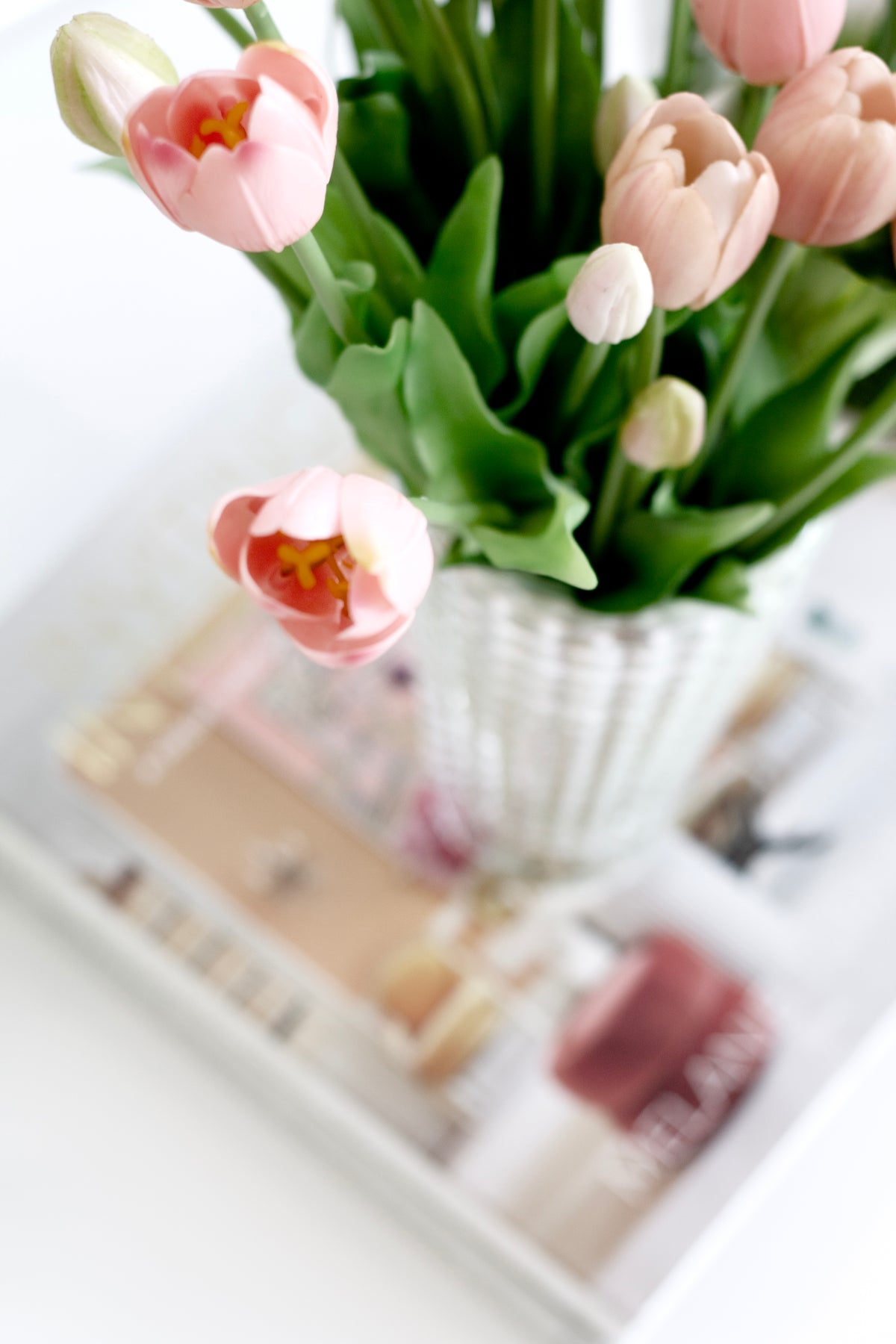 Pink and blush faux tulips in a fluted glass vase on a mirrored tray with magazines