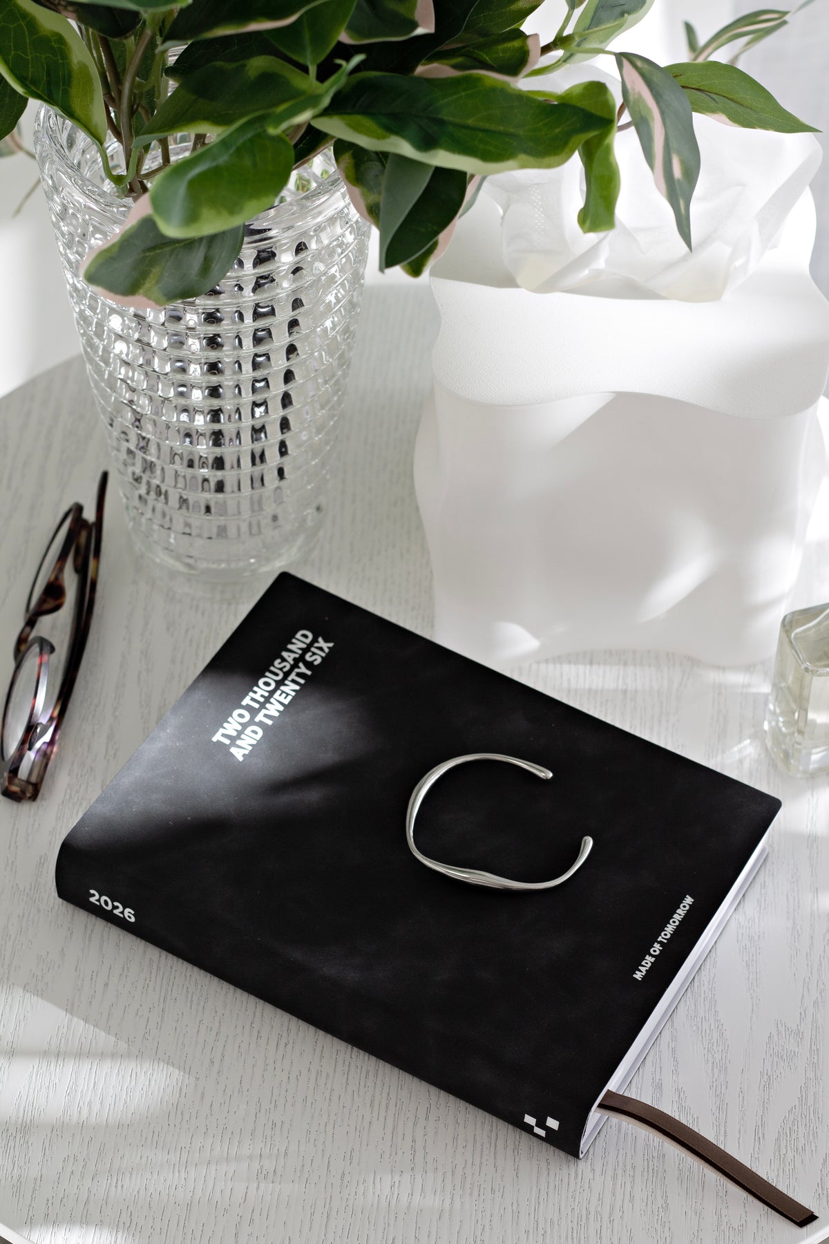 Glasses on a black book below a crystal vase of greenery