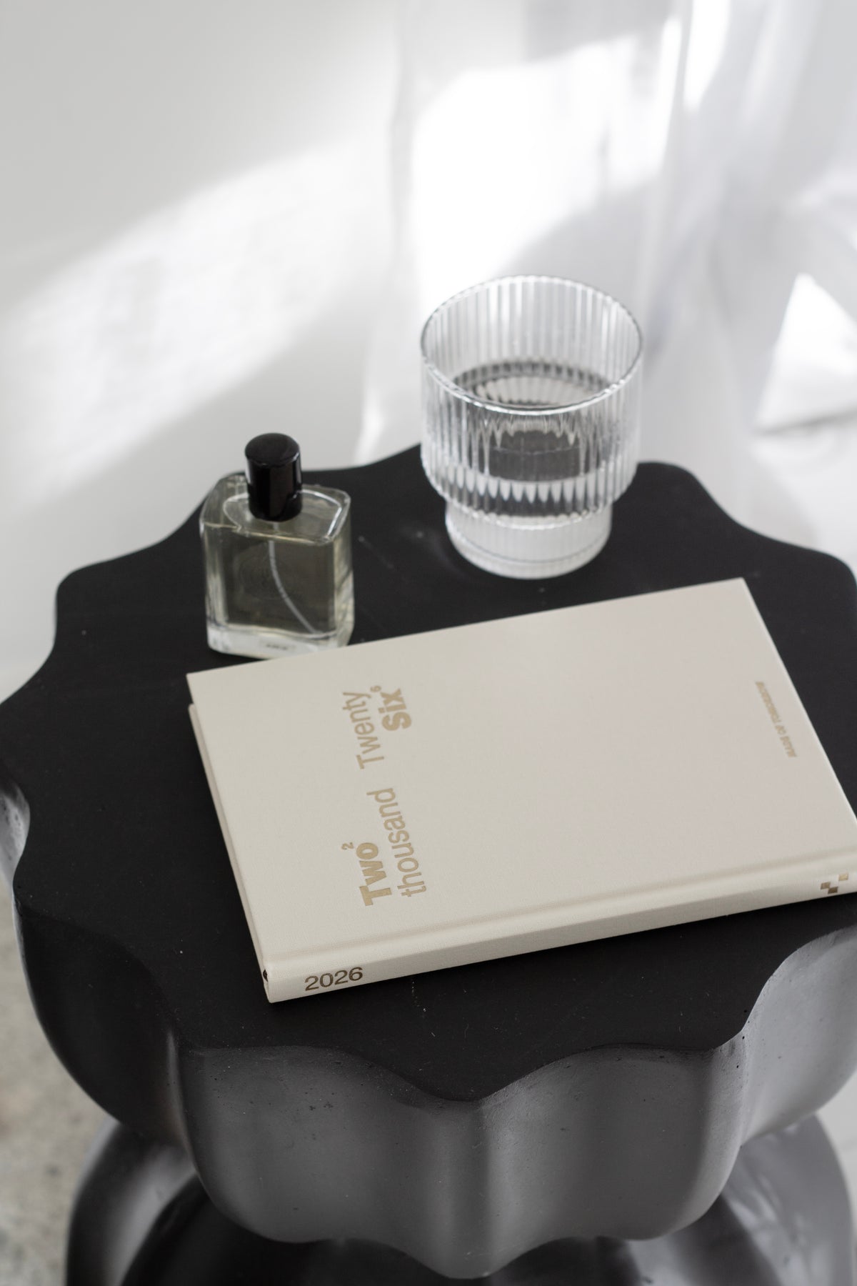 Diary, a perfume bottle and a ribbed glass on the black fluted table in bright light