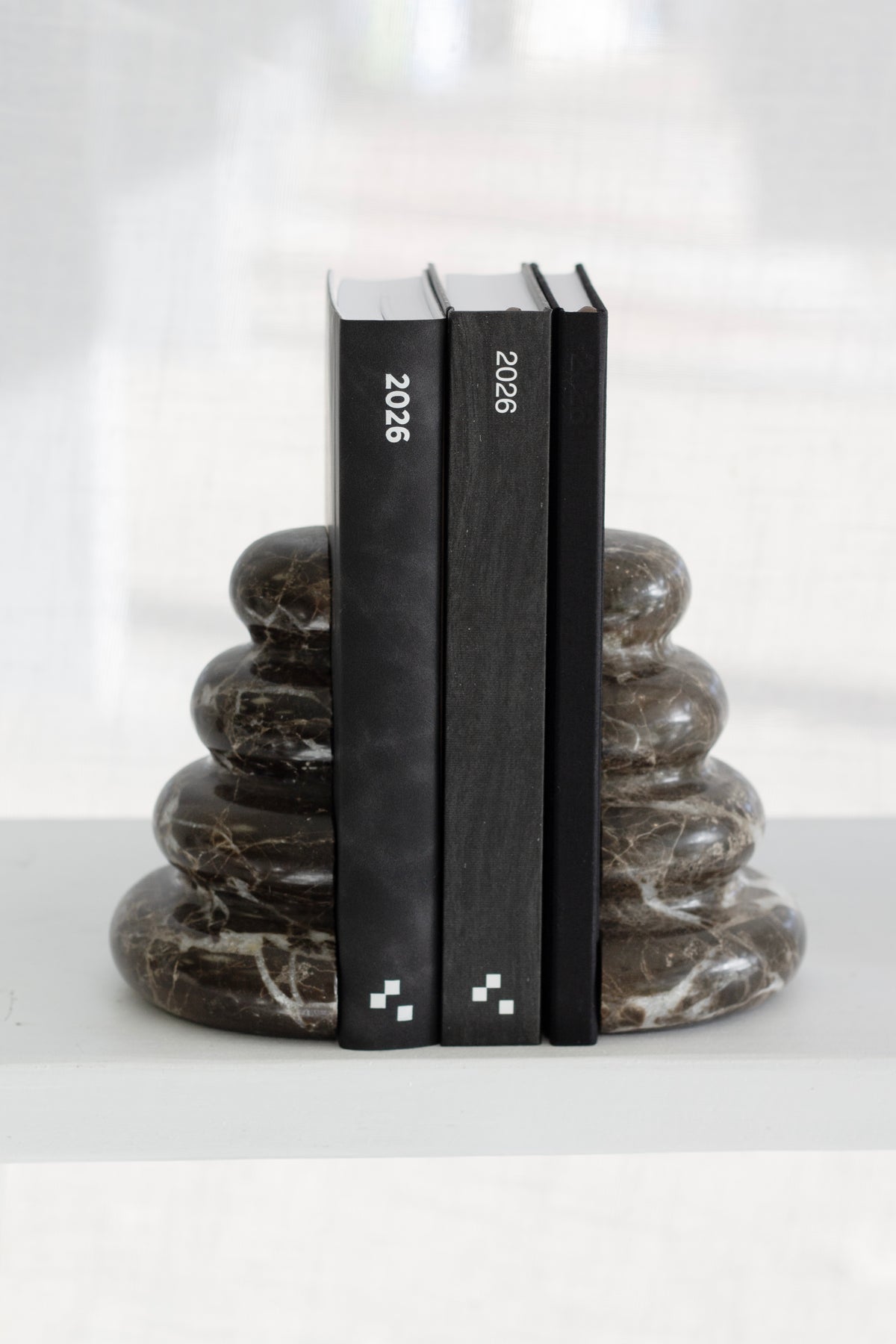 Casa bookends holding three black books on a white shelf