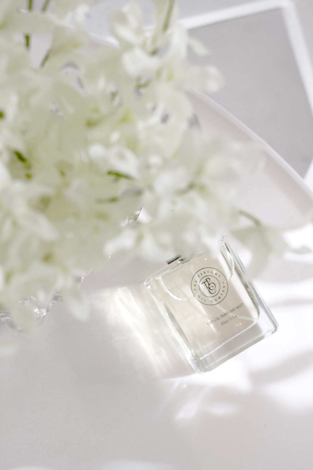 Roll-on perfume oil bottle lying on a white surface with white blossom behind