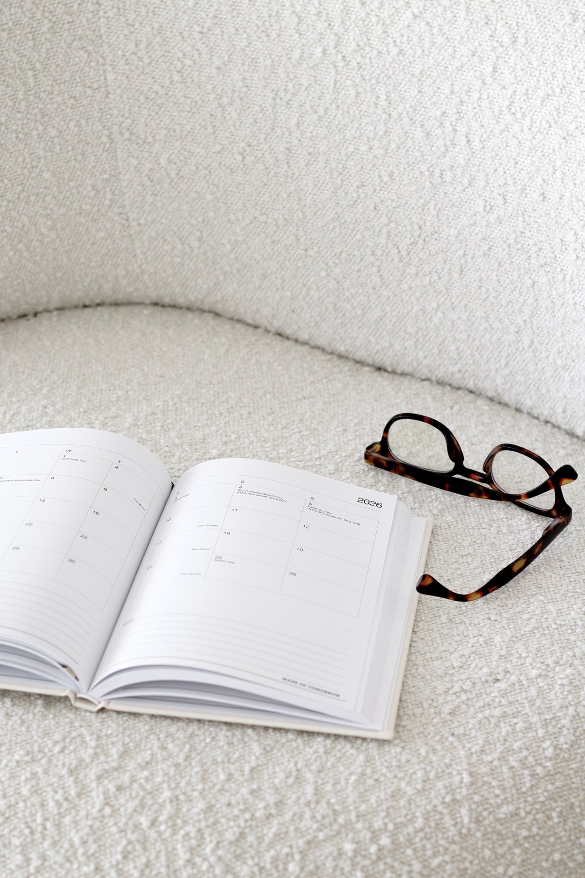 Tortoiseshell glasses on an open planner on a boucle chair