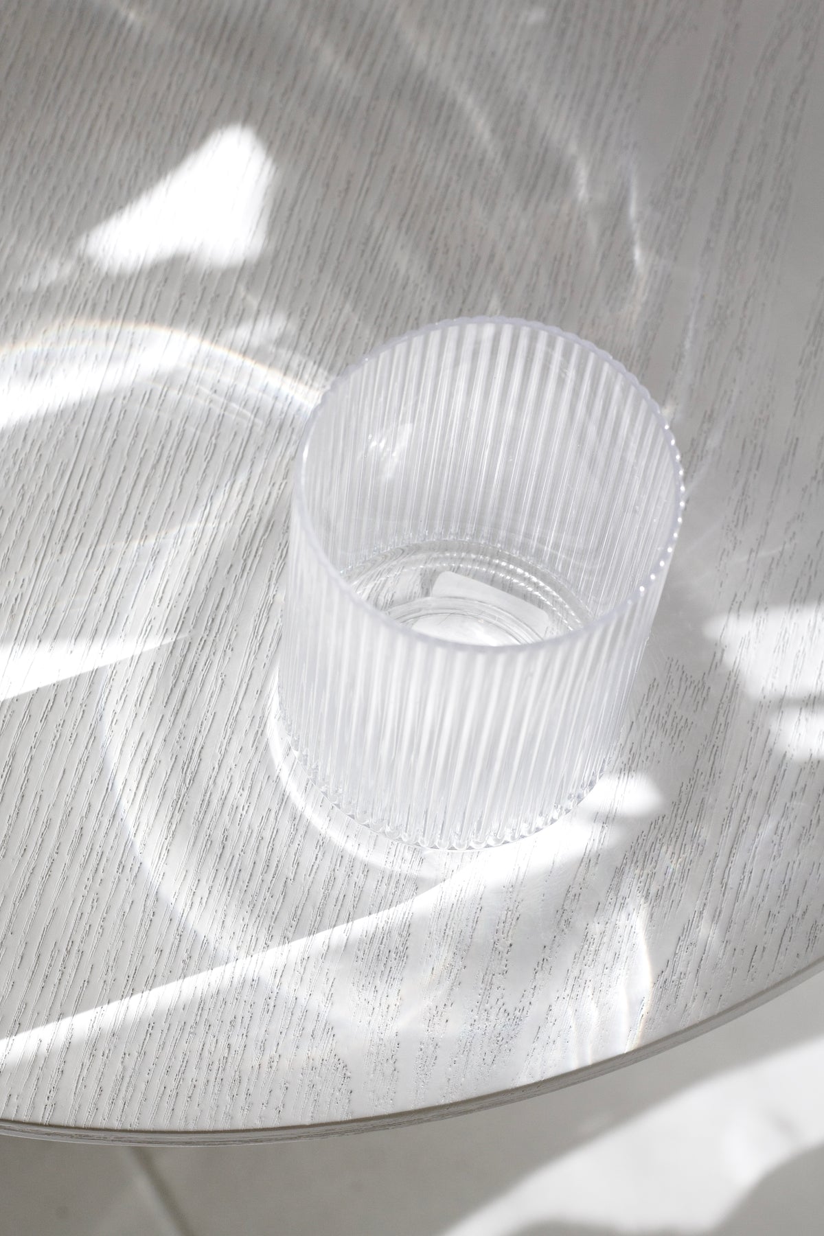 Clear fluted tumbler seen from above on a round tray, sunlight casting ribbed shadows