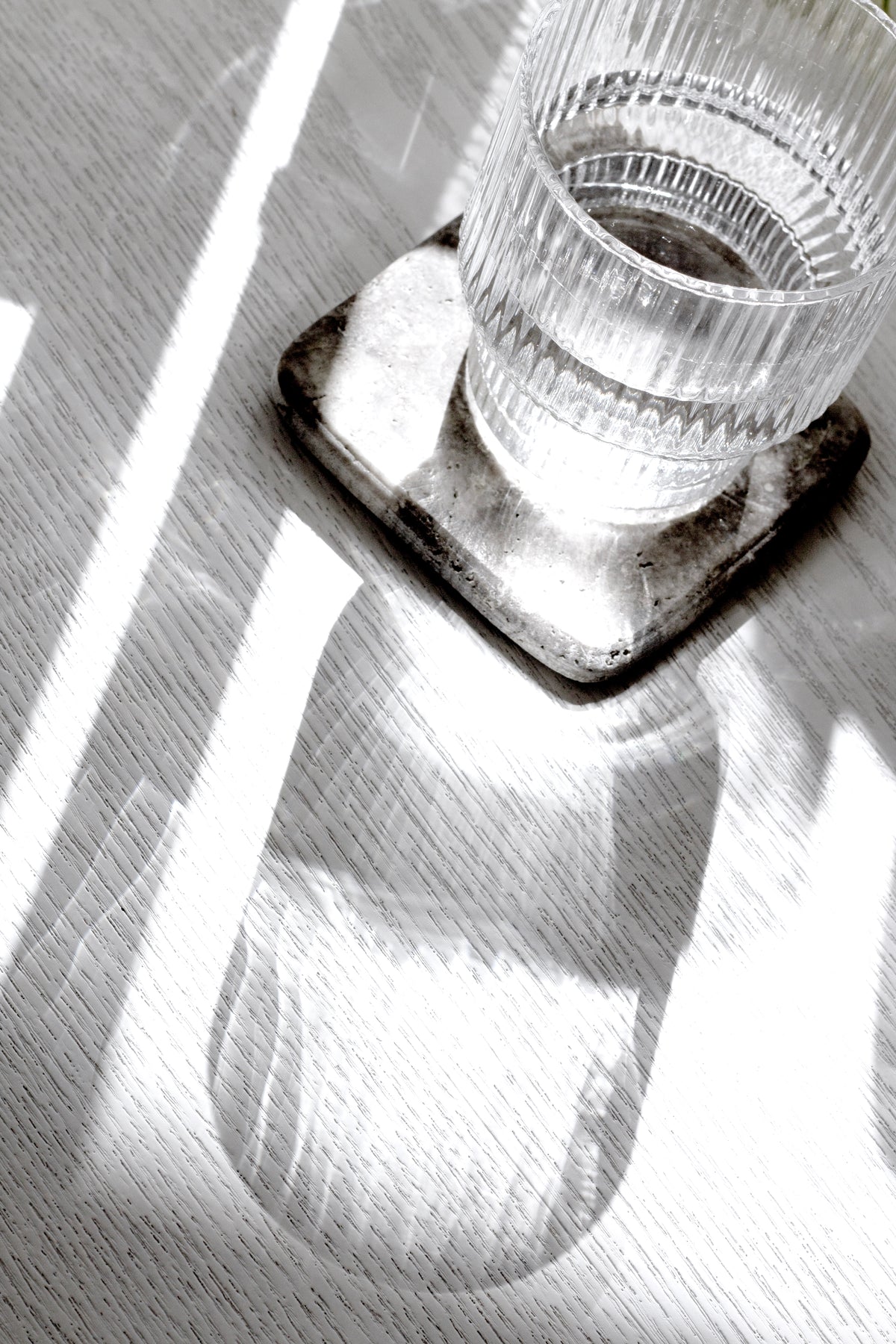 Ribbed glass on a dark marble coaster in striped sunlight