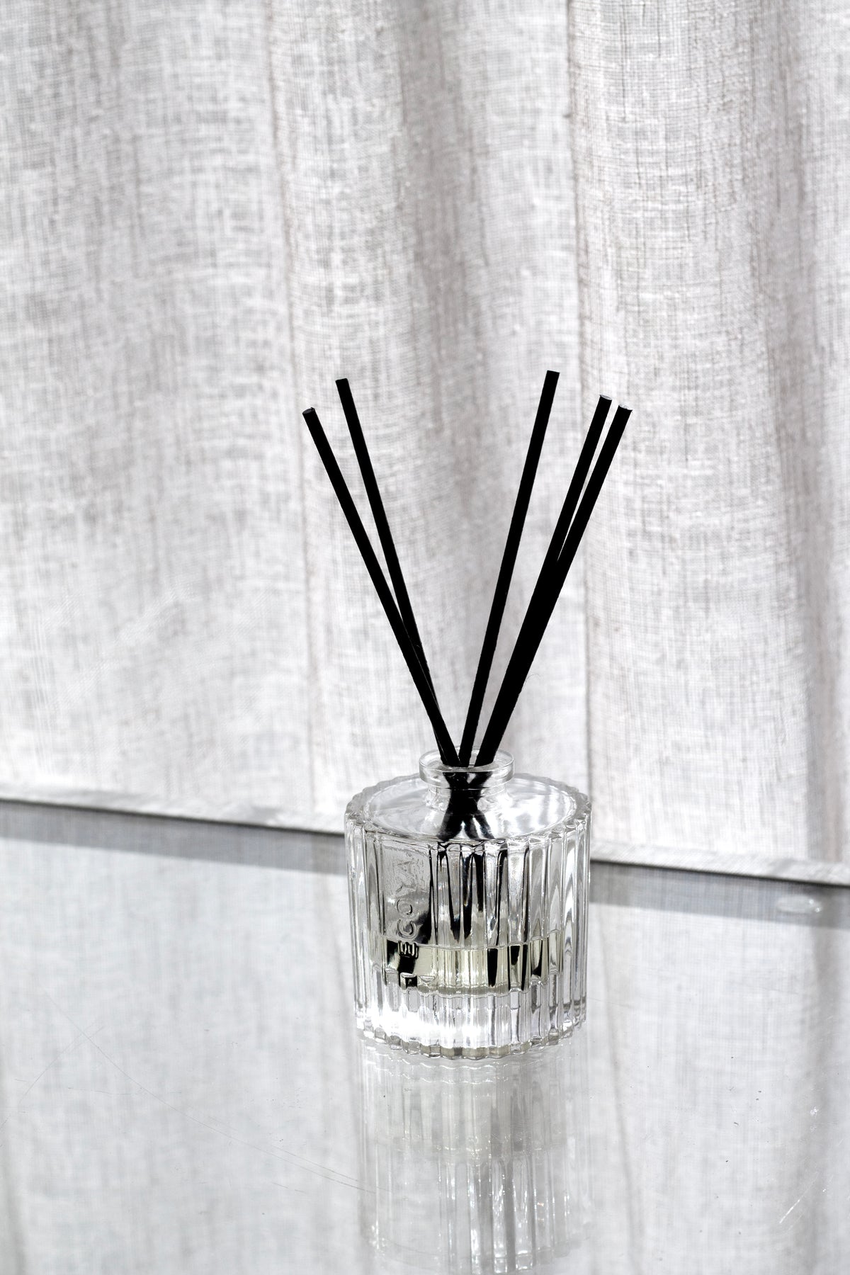 Ecoya Celebration cut glass diffuser with black reeds in front of a sheer linen curtain