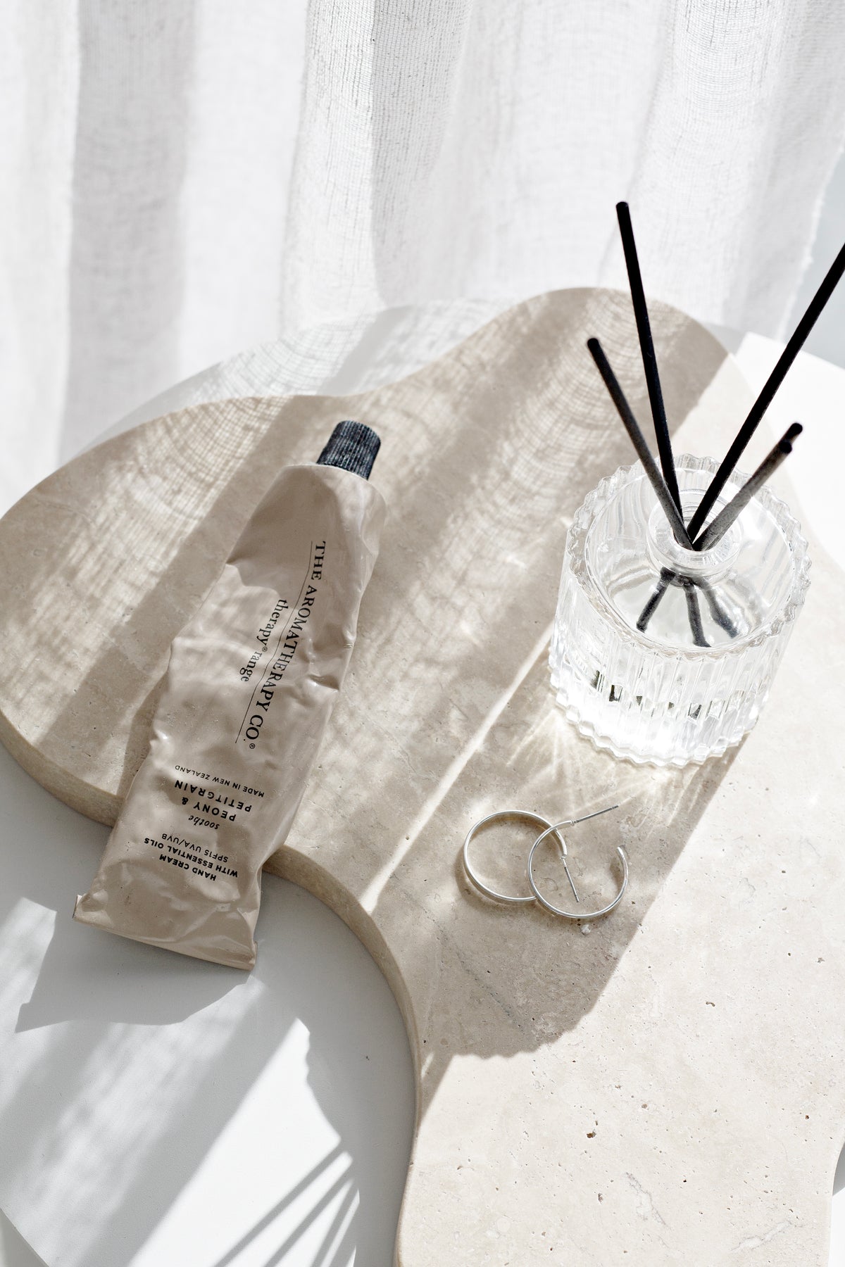 Ecoya Celebration diffuser on a stone tray with a glass bottle in soft sunlight