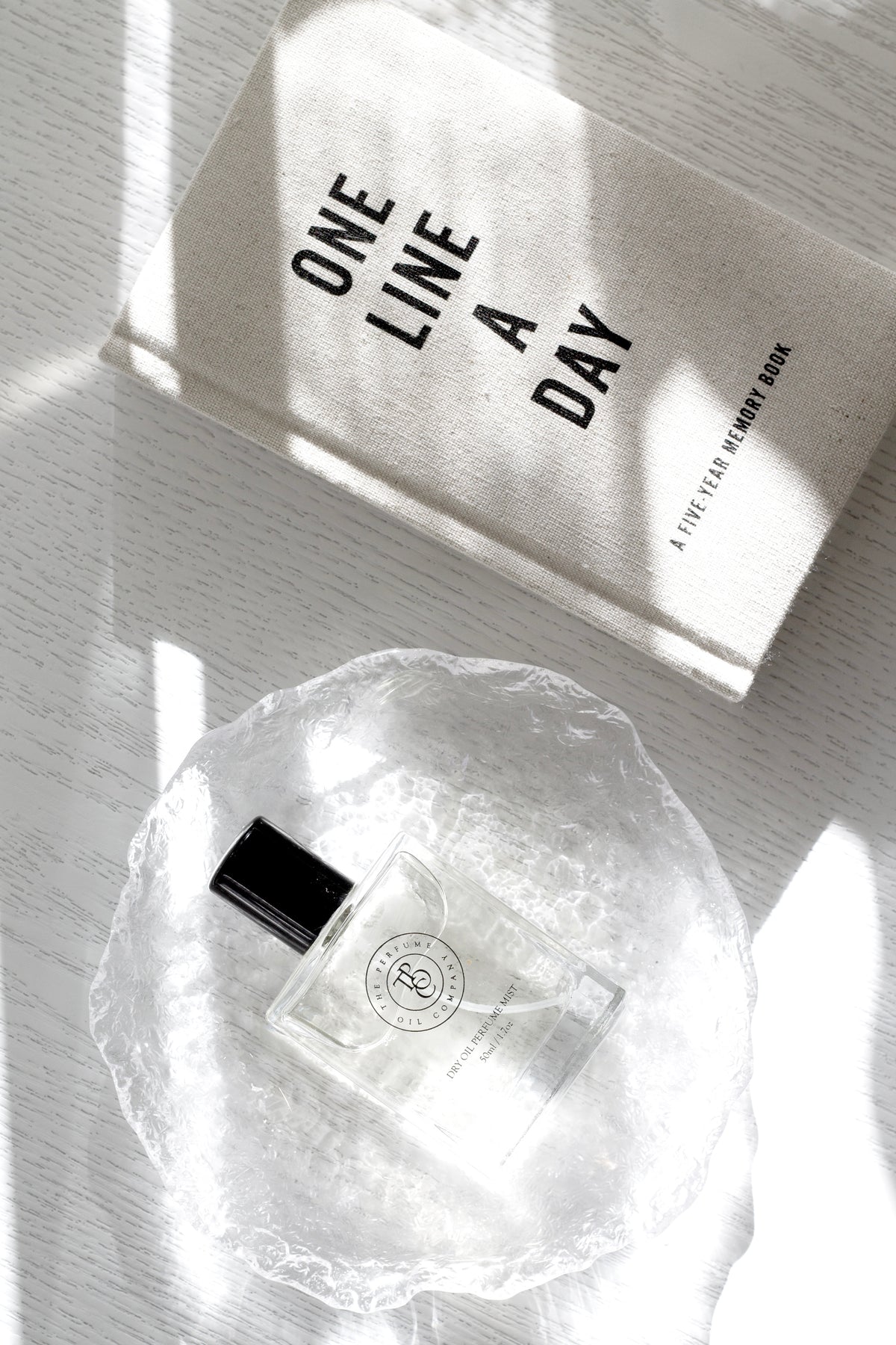 Glacier glass tray holding a small perfume bottle beside a journal in sunlight