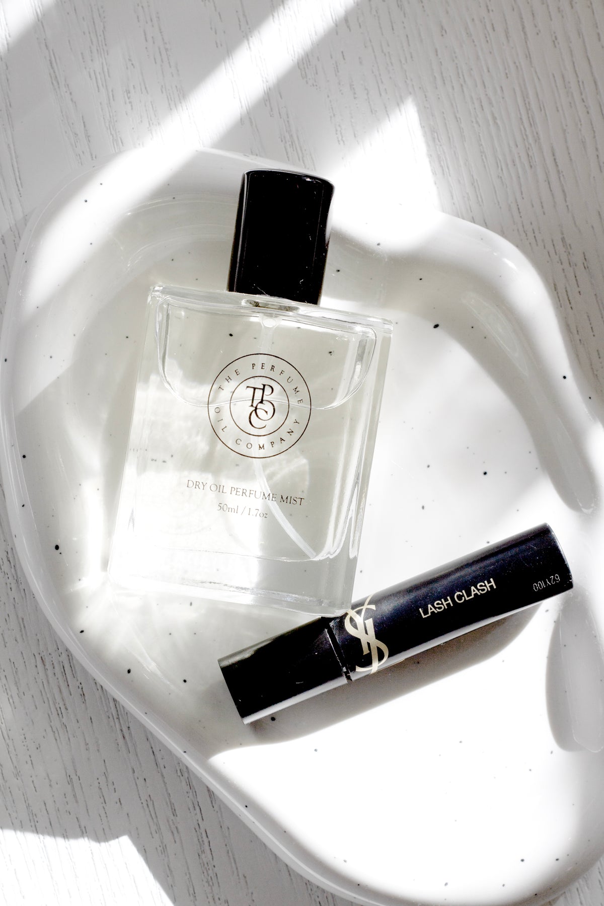 Speckled white cloud ceramic tray from above with a perfume bottle and mascara on pale timber