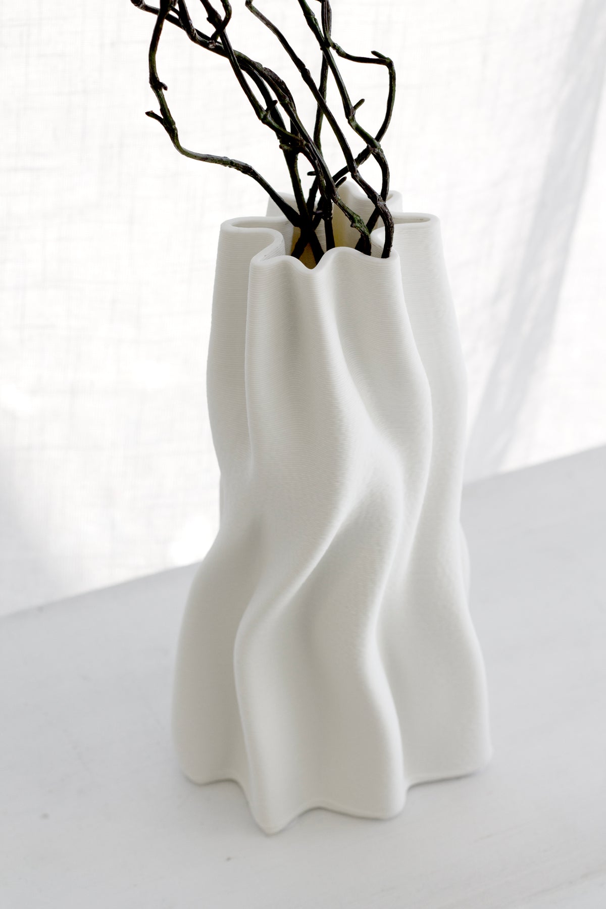 Close view of the Anouk vase's wave ridges with dark branches in soft window light
