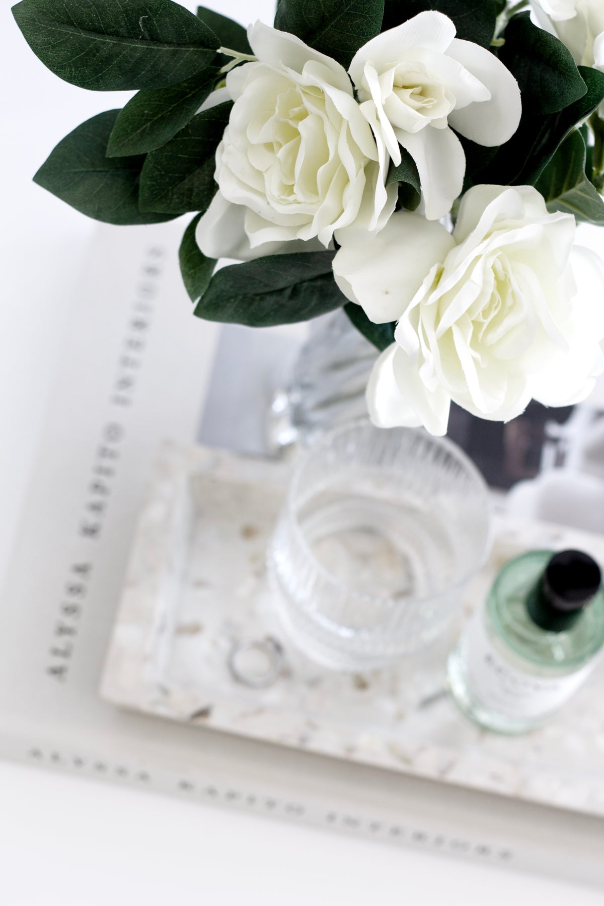 Gardenia arrangement above an interiors book with a ribbed tumbler and fragrance bottle