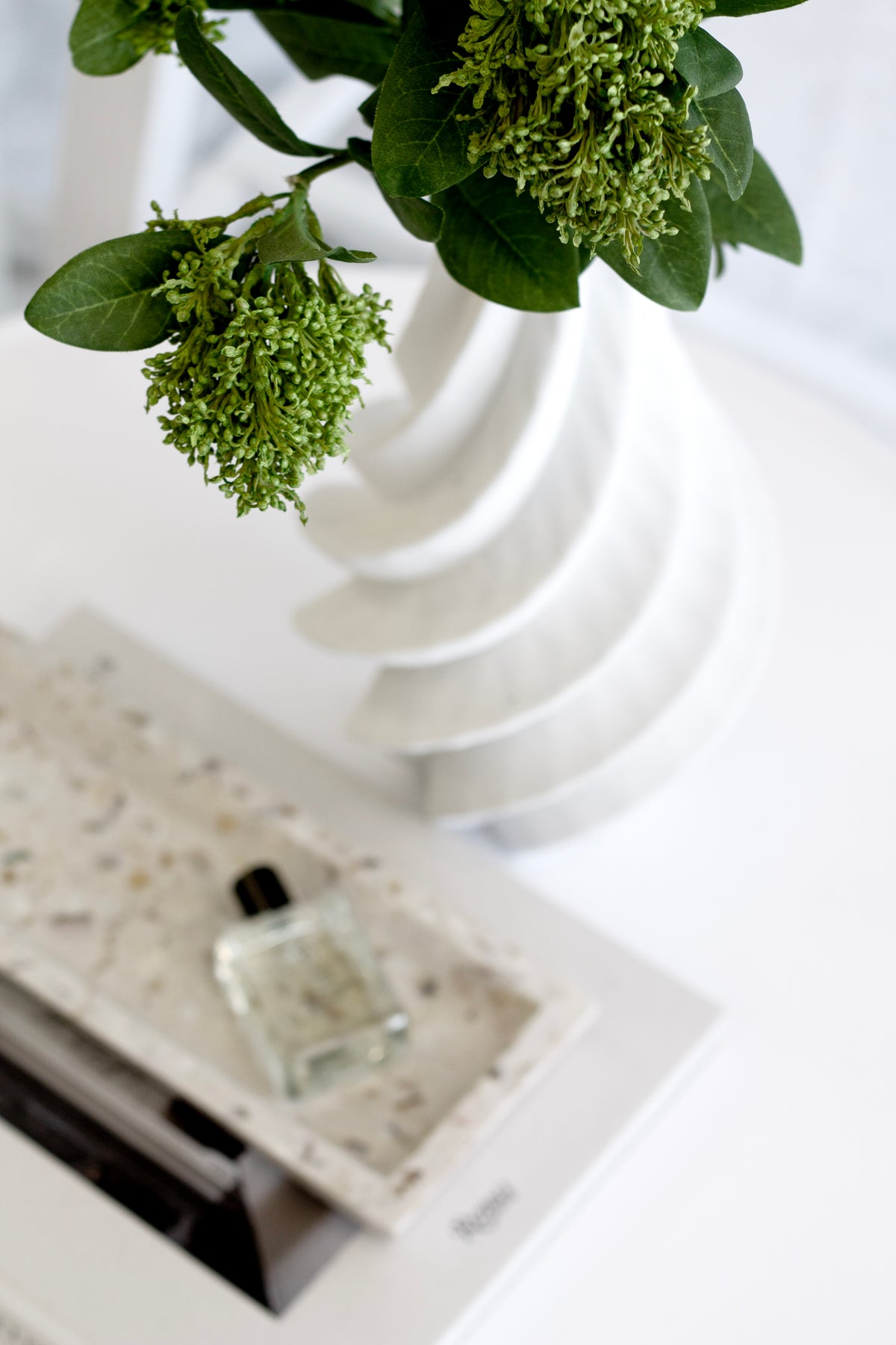 Green blossom stems in the spiral vase above a terrazzo tray holding a small bottle