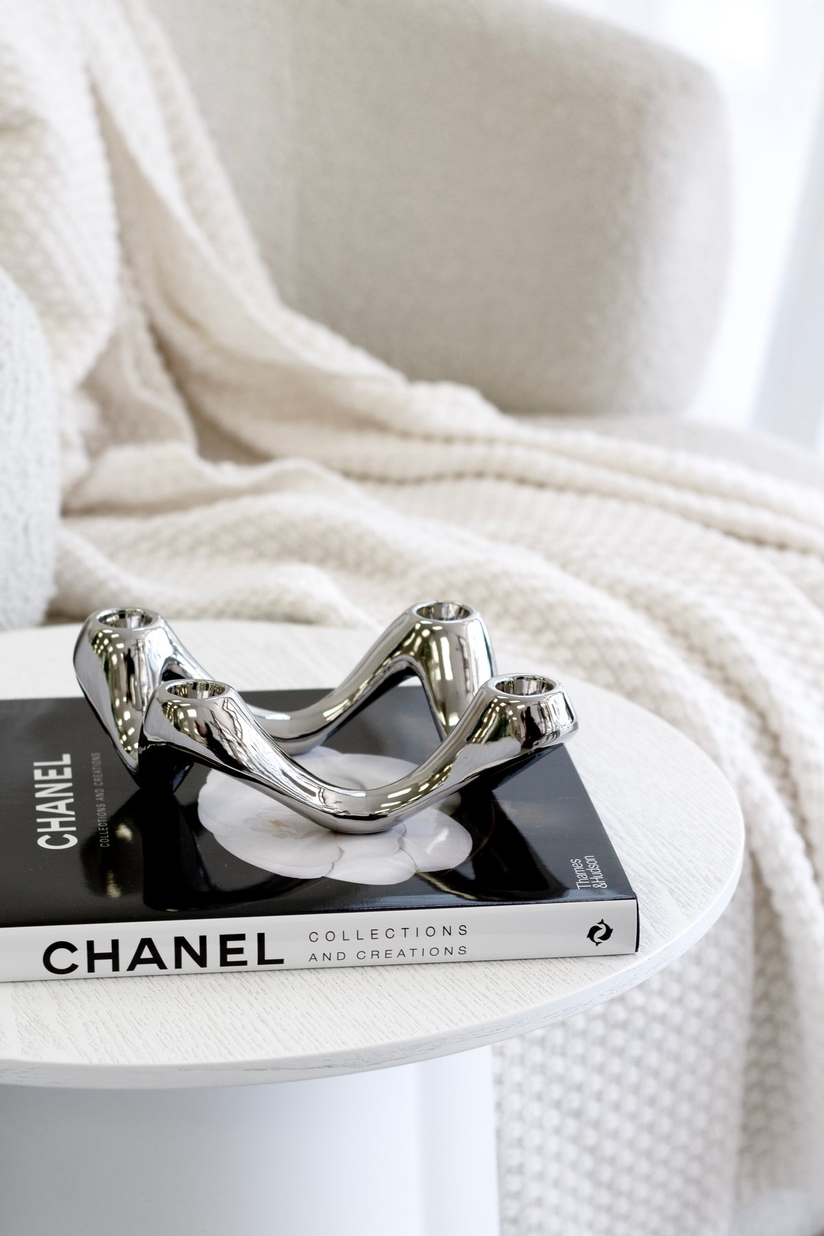 Silver candle holder on a book at the edge of a round white table, waffle throw behind