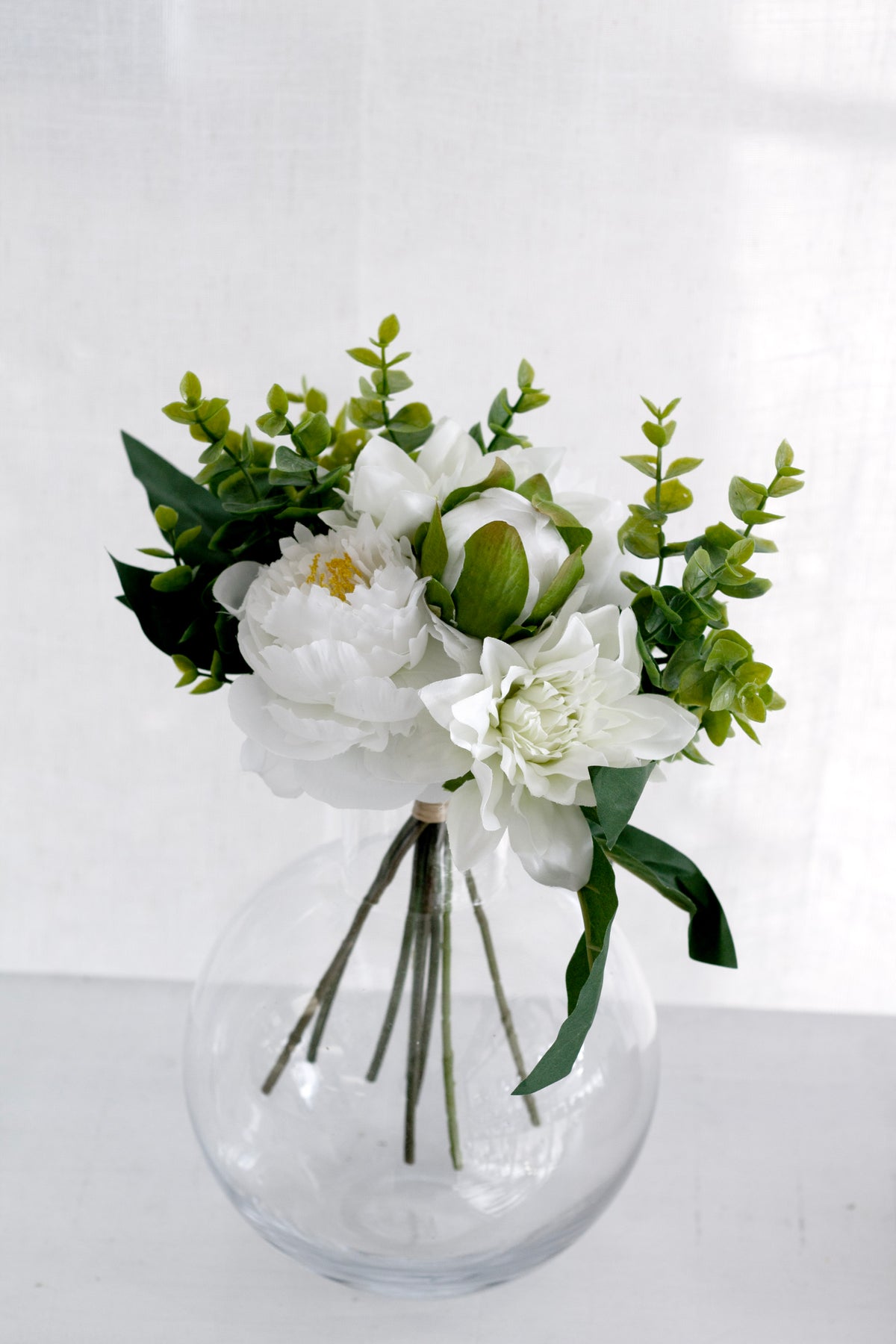 Dahlia and peony bouquet in a round glass vase