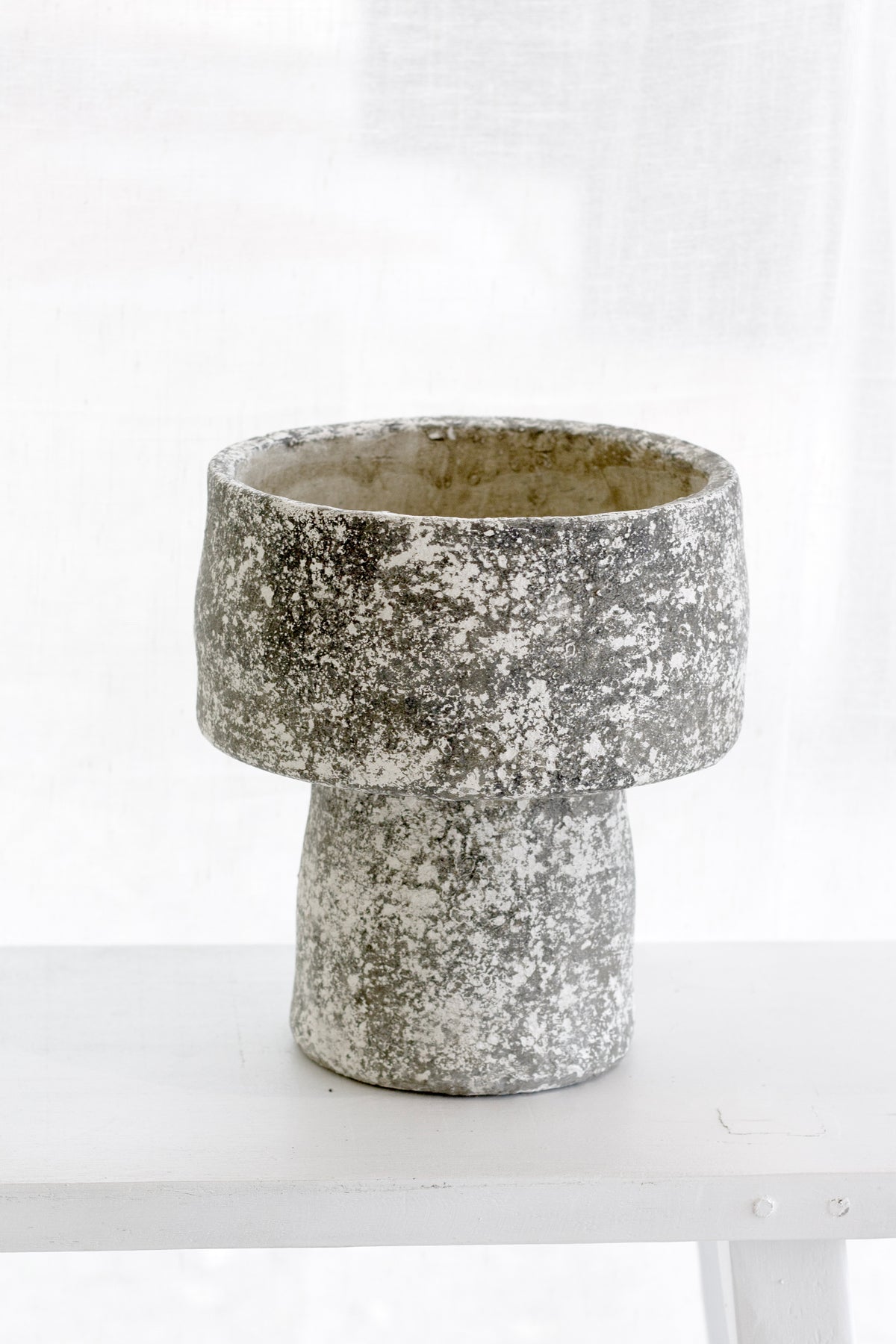 Grey wash cement mushroom planter on a white table beside a sheer curtain