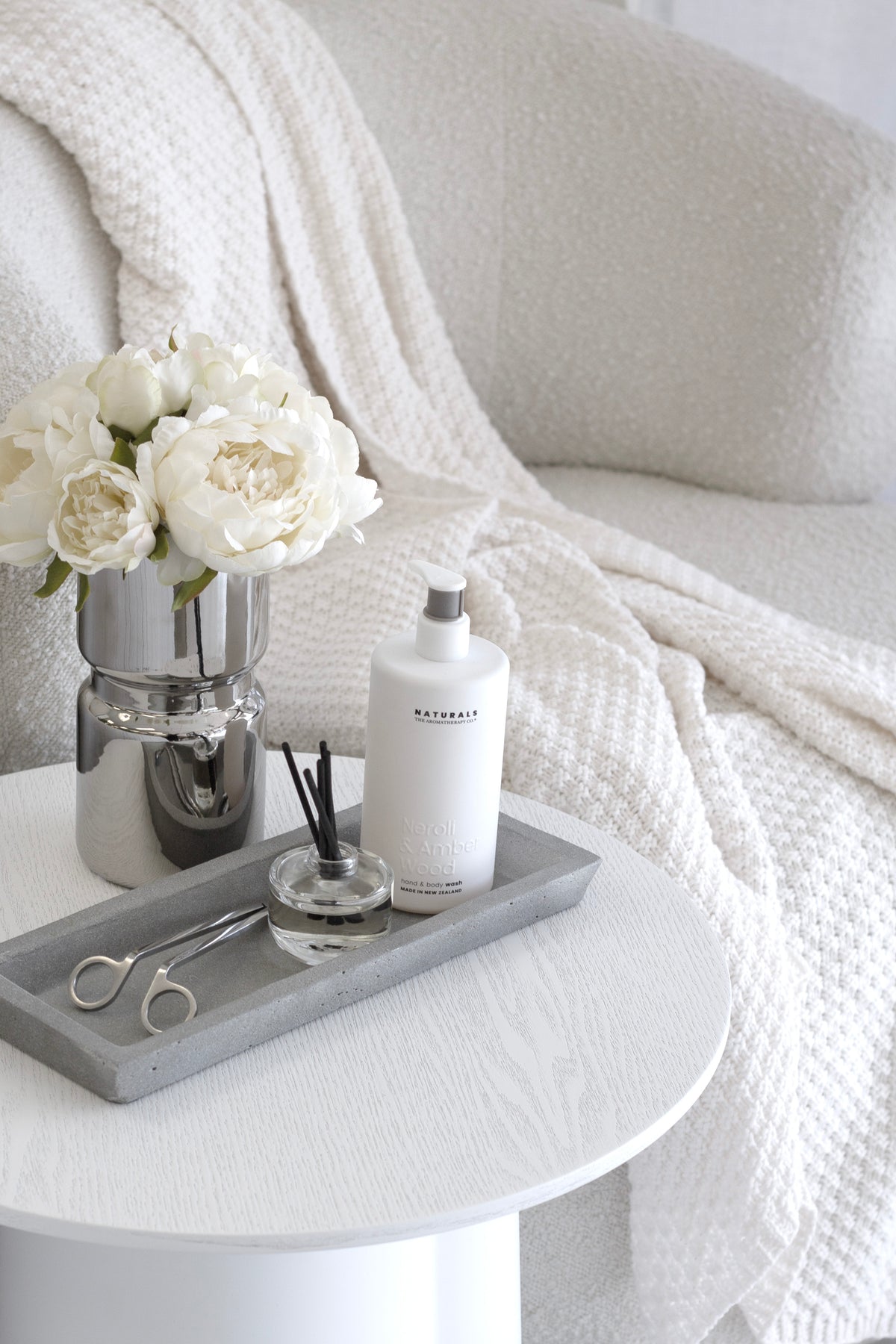 Silver vase of white peonies on a round table with a waffle throw behind