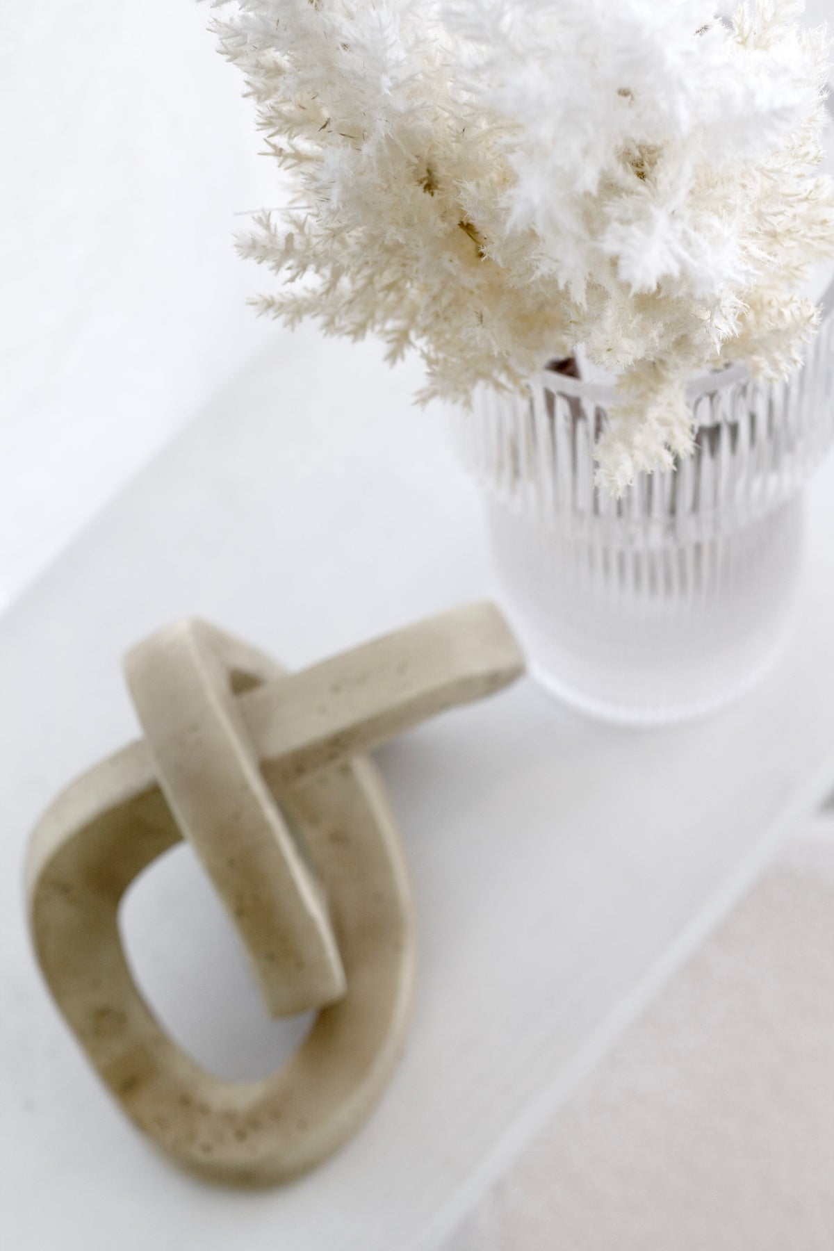 Cream astilbe in a fluted glass vase on a white tray with a stone chain link ornament
