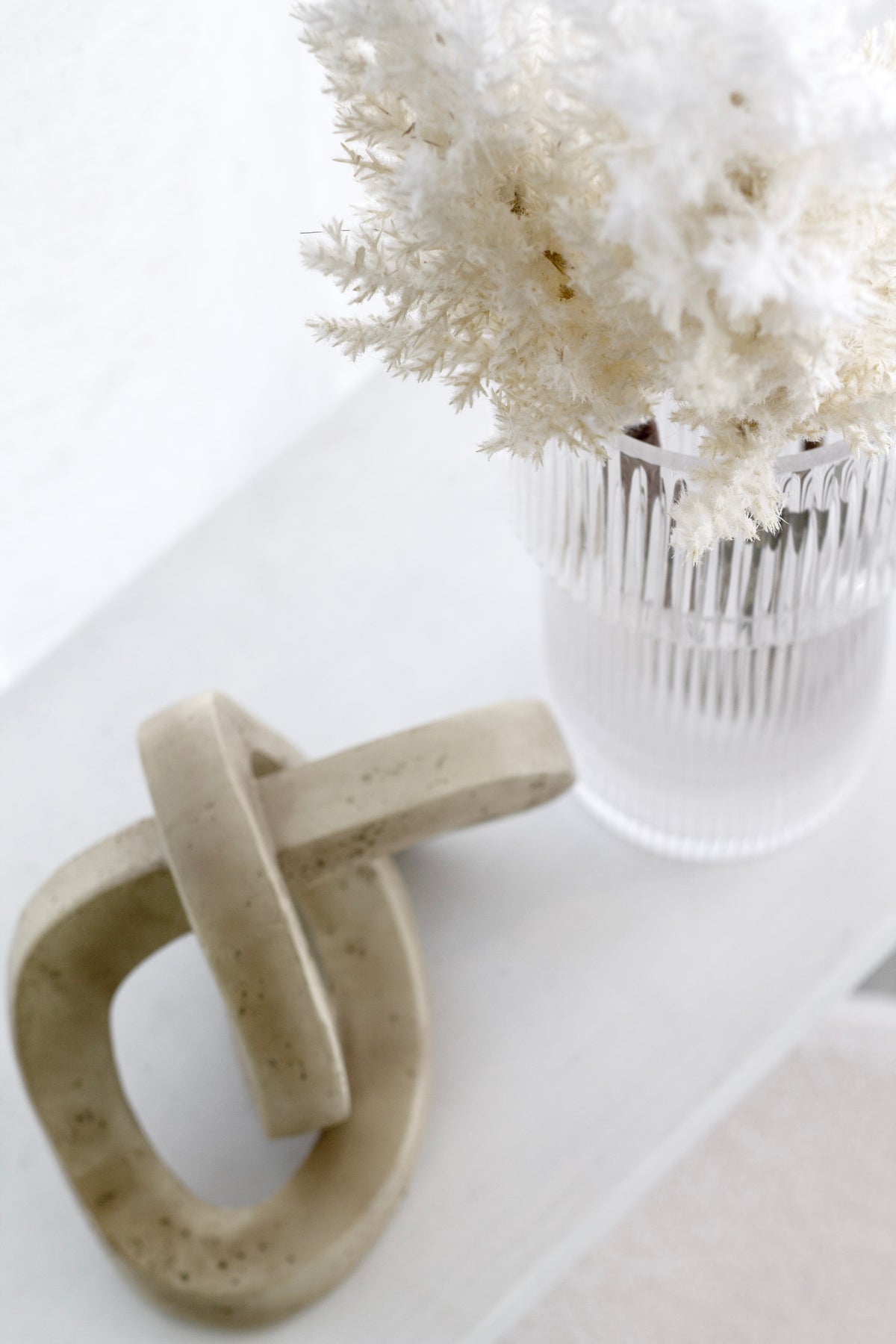 Cream astilbe and dried botanicals in a fluted glass vase beside a stone chain link ornament
