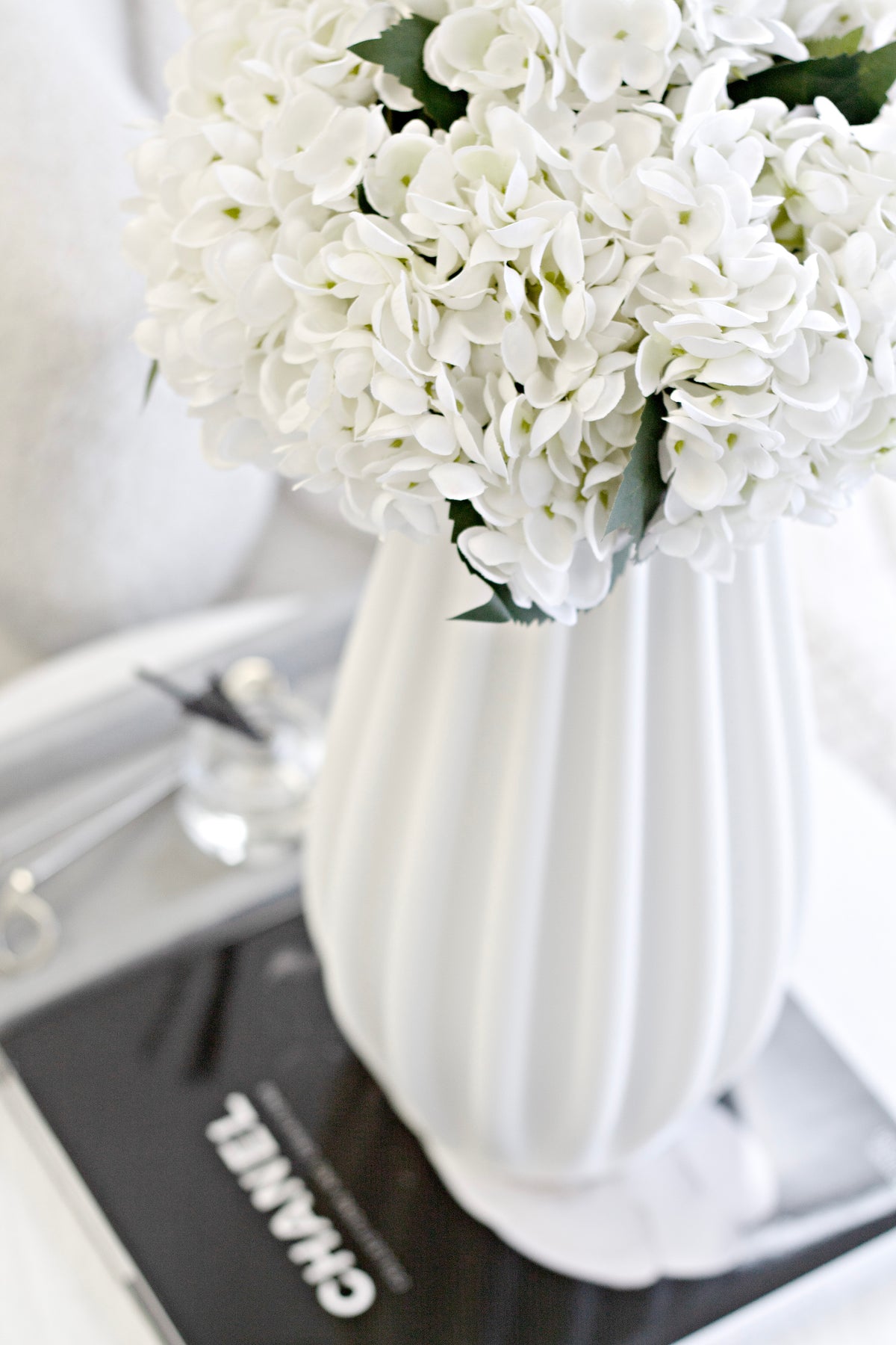 The fluted vase of hydrangeas on a black book with a knit throw behind