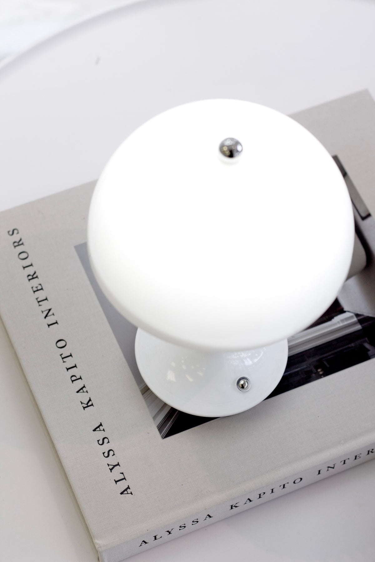 White mushroom lamp unlit, seen from above resting on an interiors book