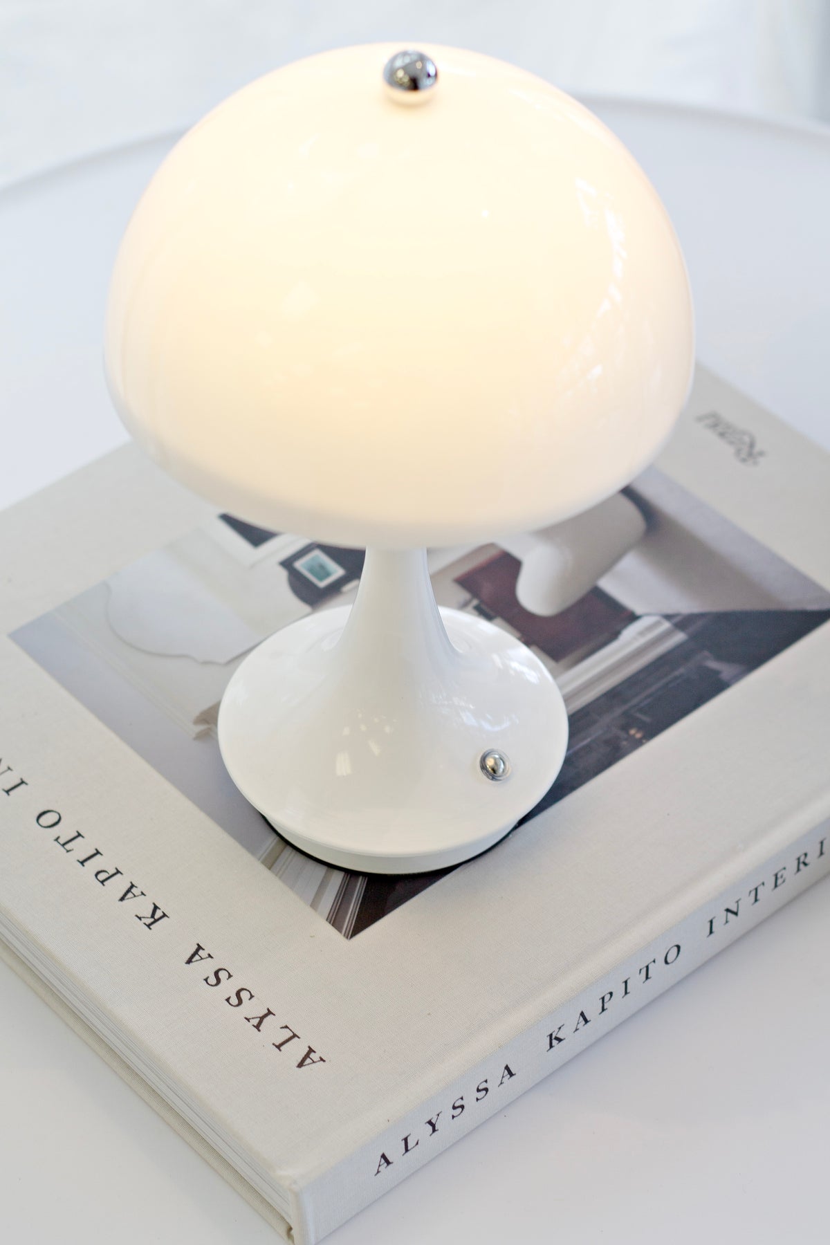 White mushroom lamp lit, resting on an interiors book at close range