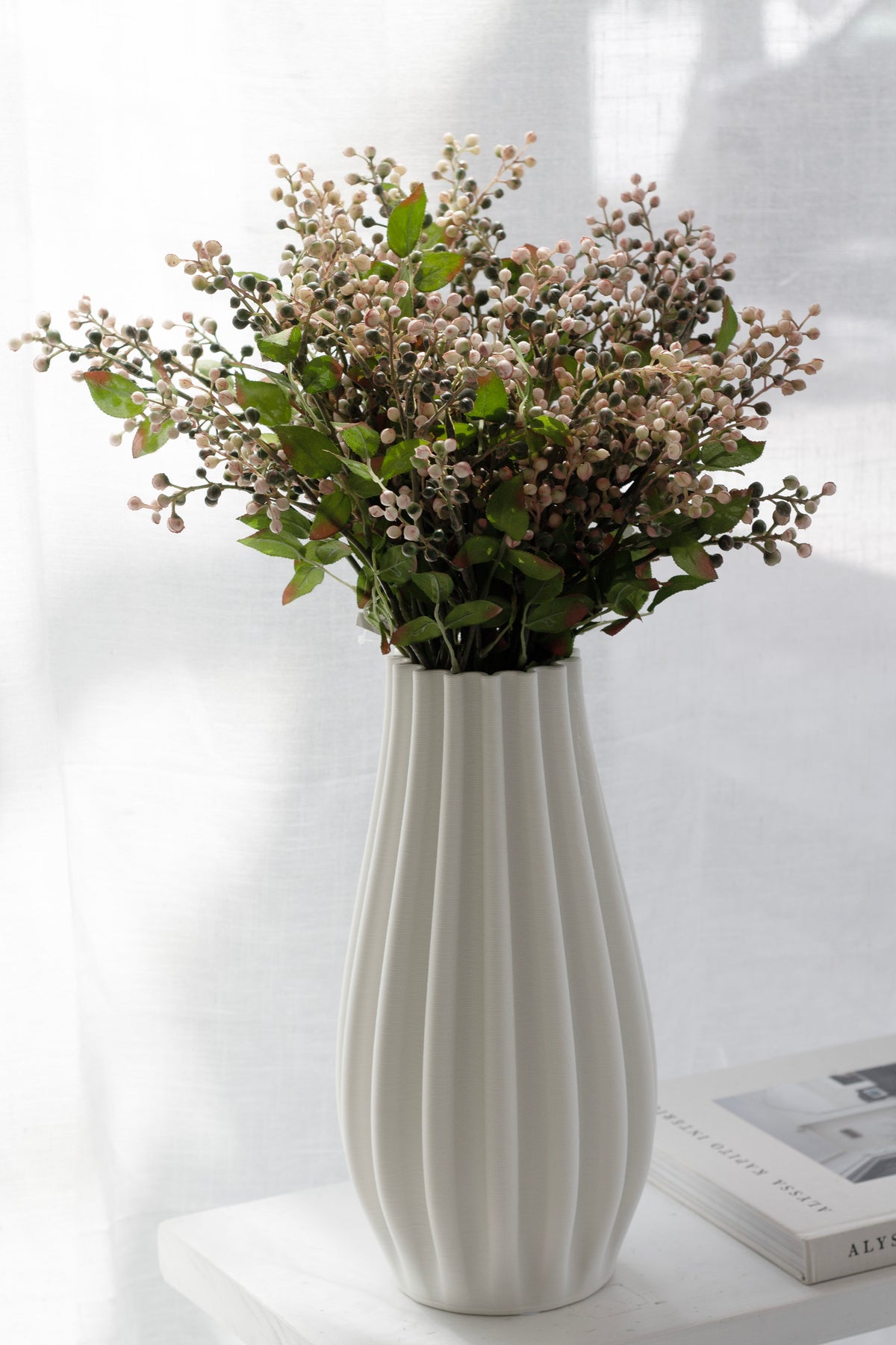 Cottage berry spray in a white fluted vase on a side table beside a book
